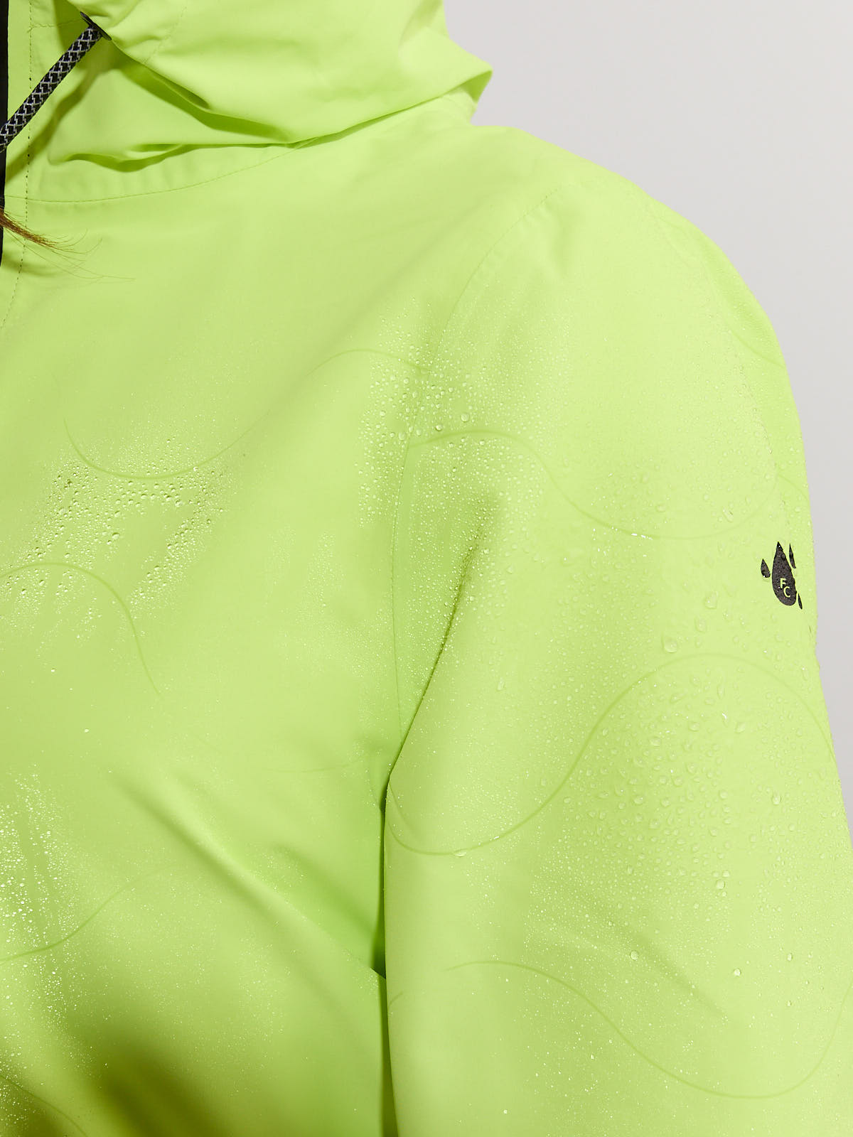 Close-up of a neon green waterproof jacket with water droplets on the surface and a small black logo on the sleeve