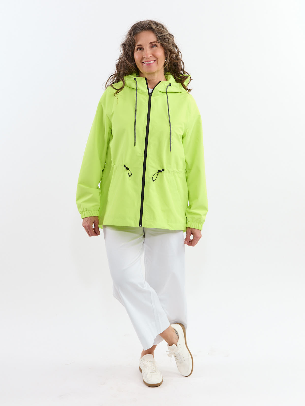 Person wearing a bright green hooded jacket with black drawstrings and white pants standing against a white background.