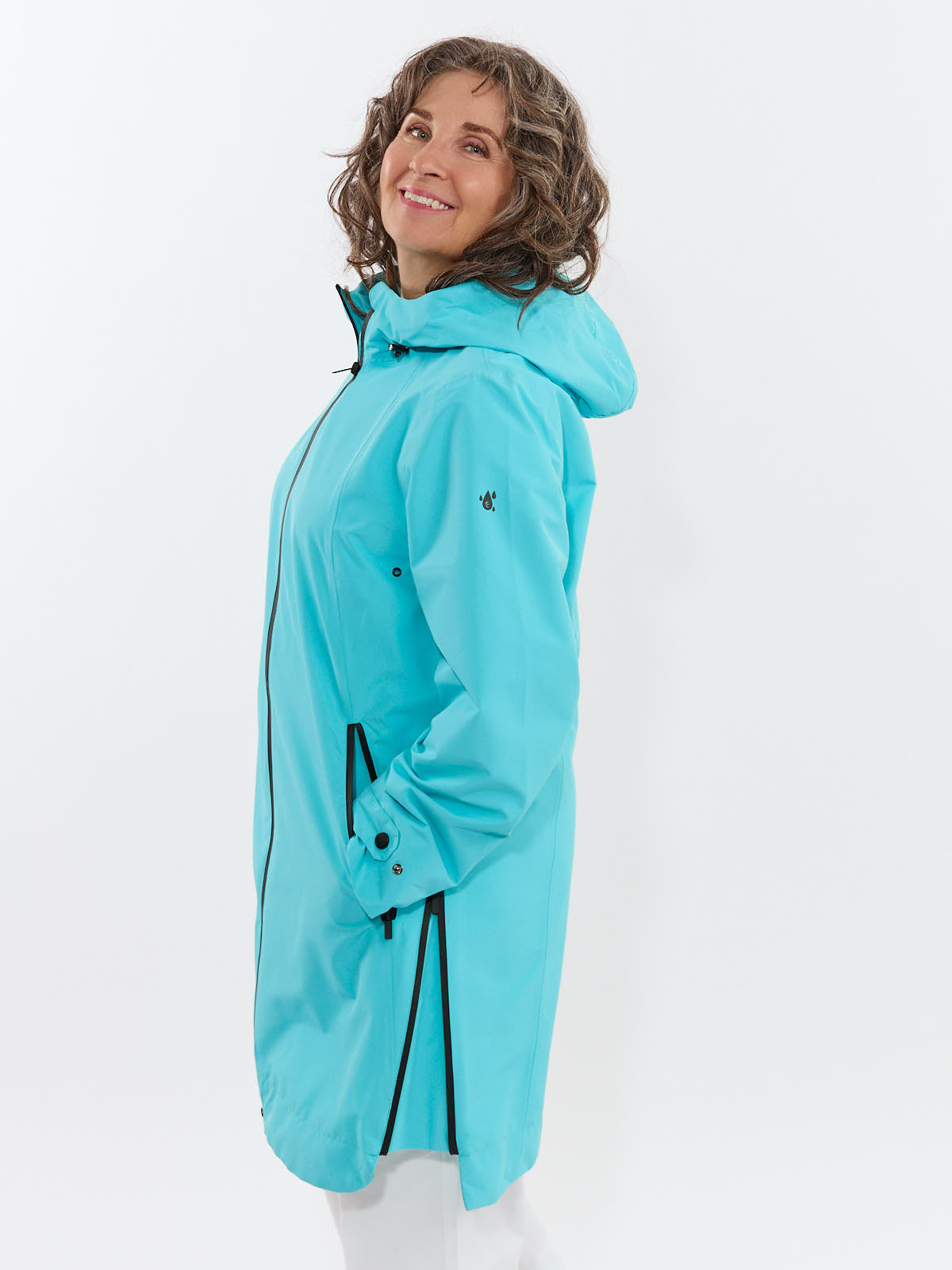 Smiling person wearing a bright aqua hooded raincoat with zippered pockets and adjustable cuffs against white background
