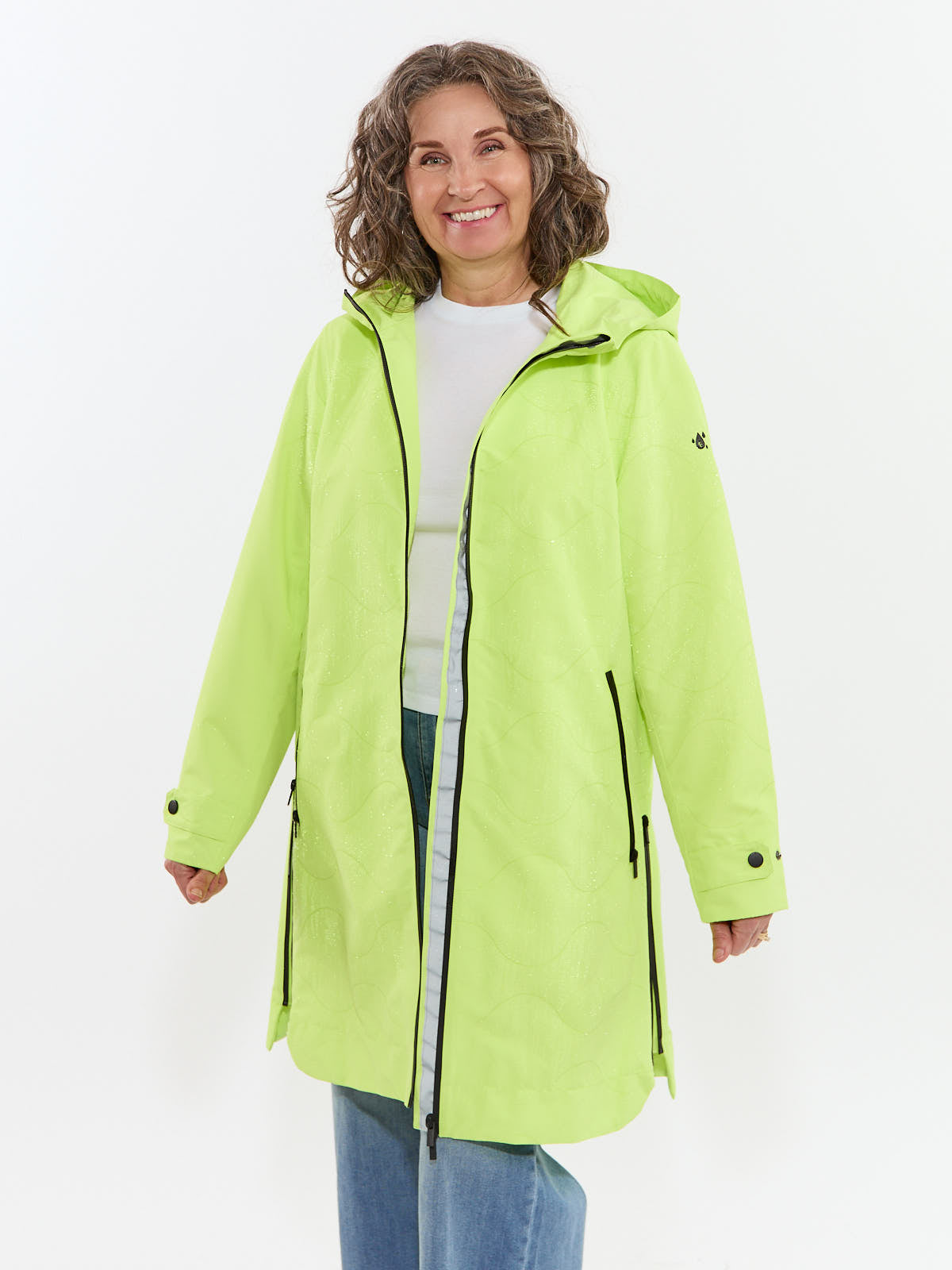 Smiling individual wearing a light green hooded jacket with zipper details over a white top and jeans.