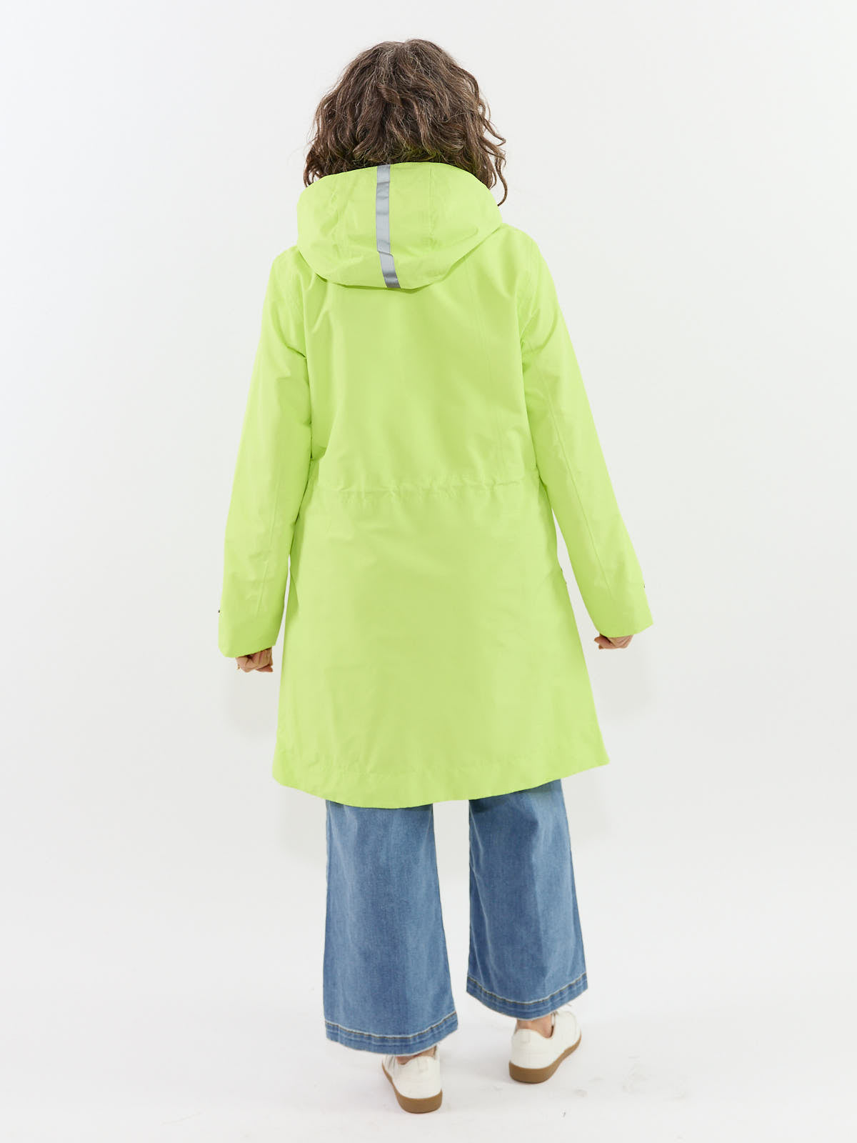 Person wearing a lime green hooded raincoat with reflective strip on hood and wide-leg blue denim jeans viewed from back