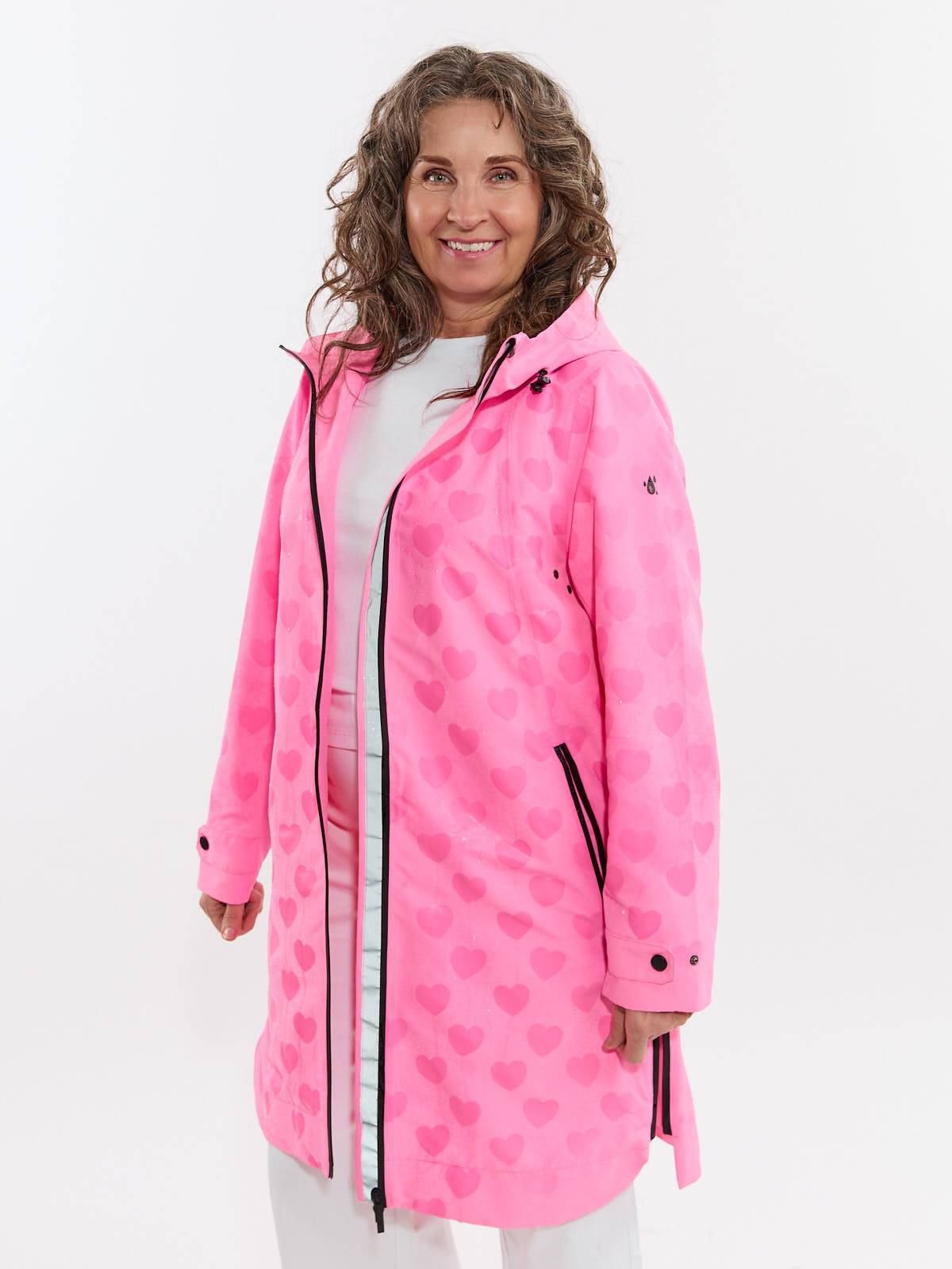 Smiling person wearing a long pink hooded coat with a subtle heart pattern and black zipper details.