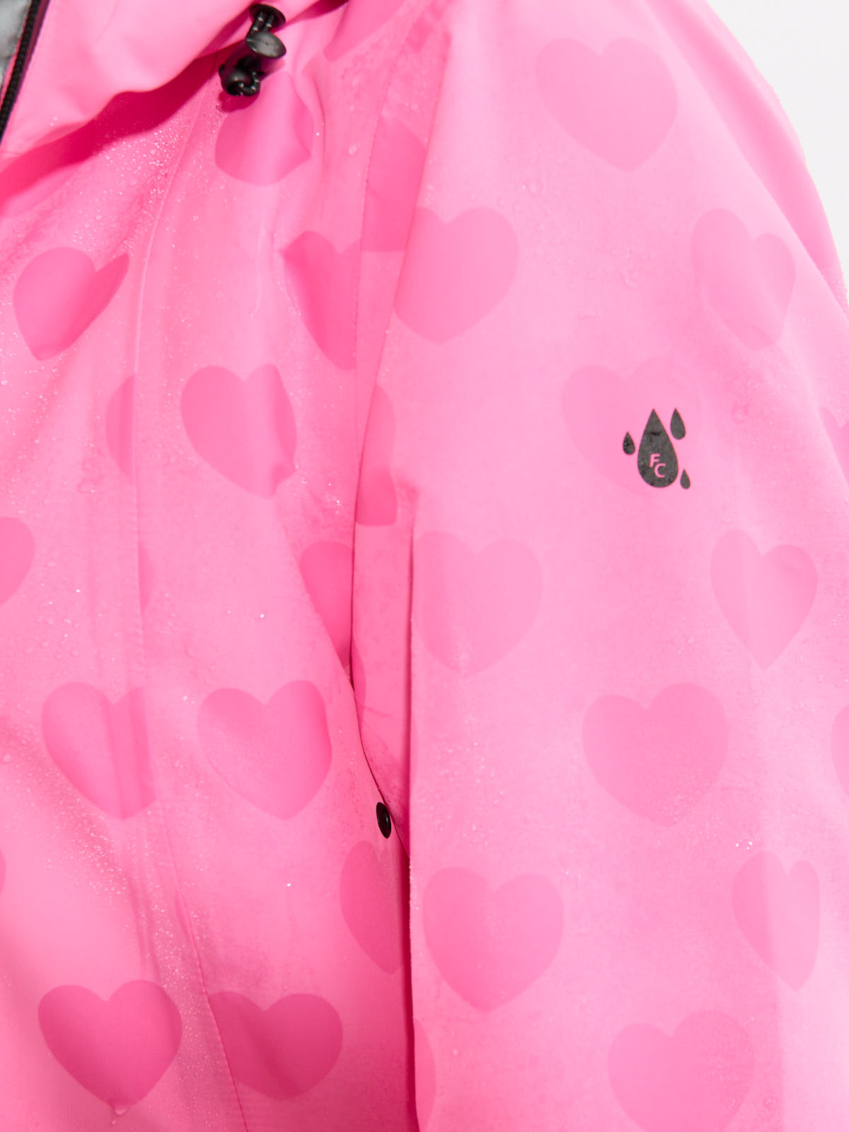 Close-up of a pink waterproof jacket with a heart pattern and a small black water droplet logo on the sleeve.