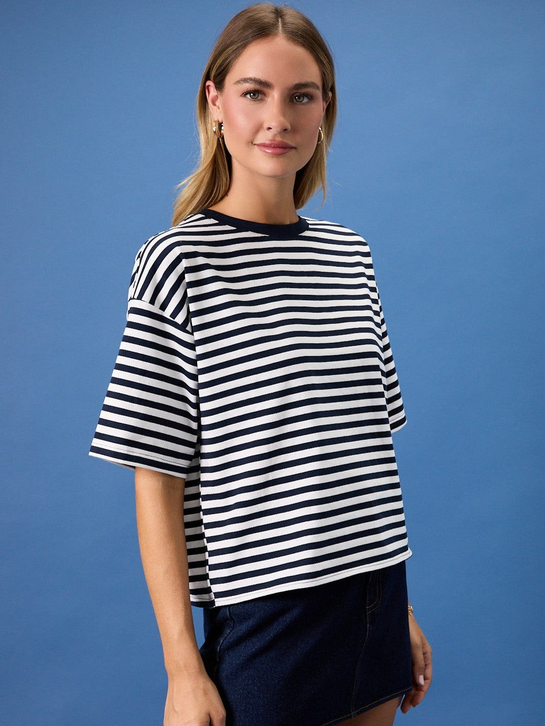 Striped navy and white short-sleeve top paired with a dark denim skirt against a solid blue background