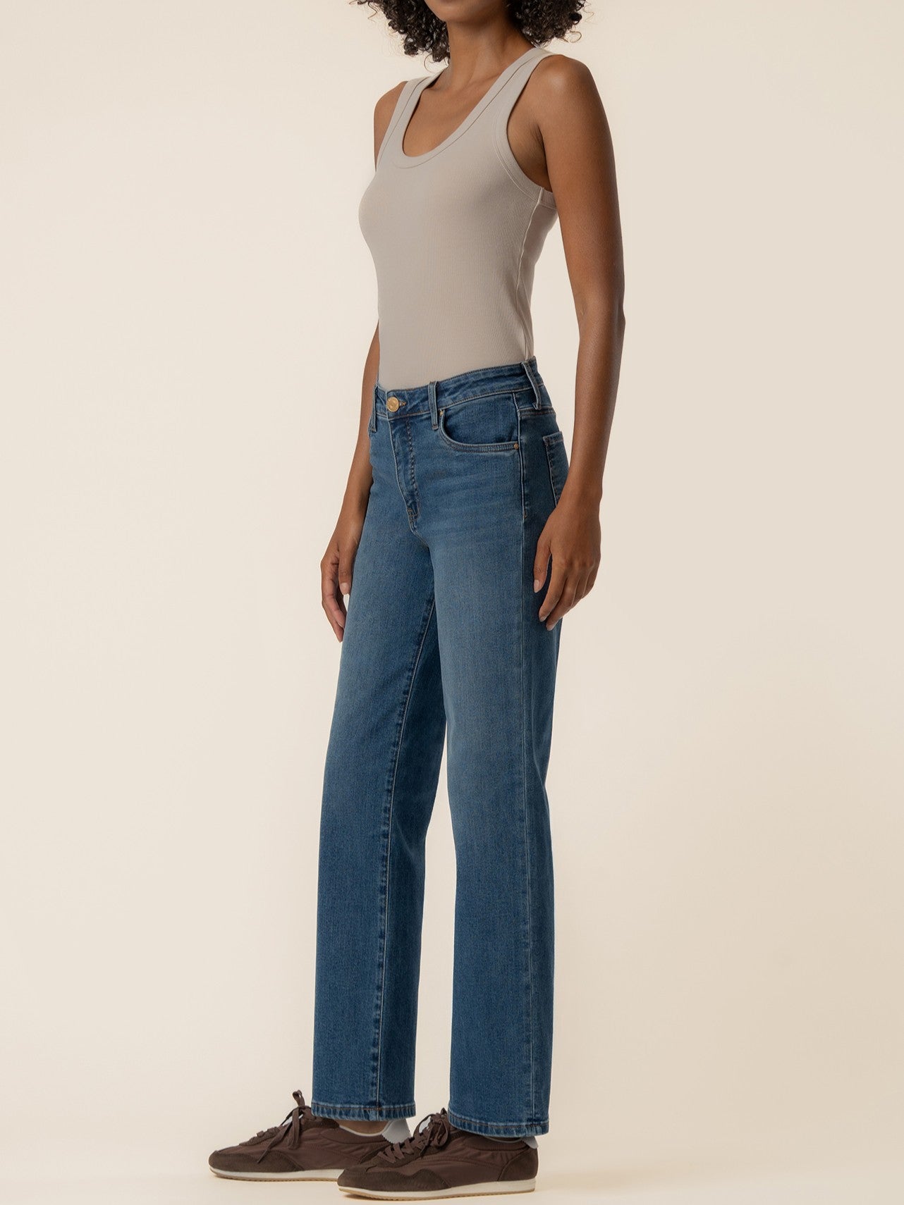 Side view of a sleeveless beige top paired with medium-wash straight-leg denim jeans and dark casual shoes.