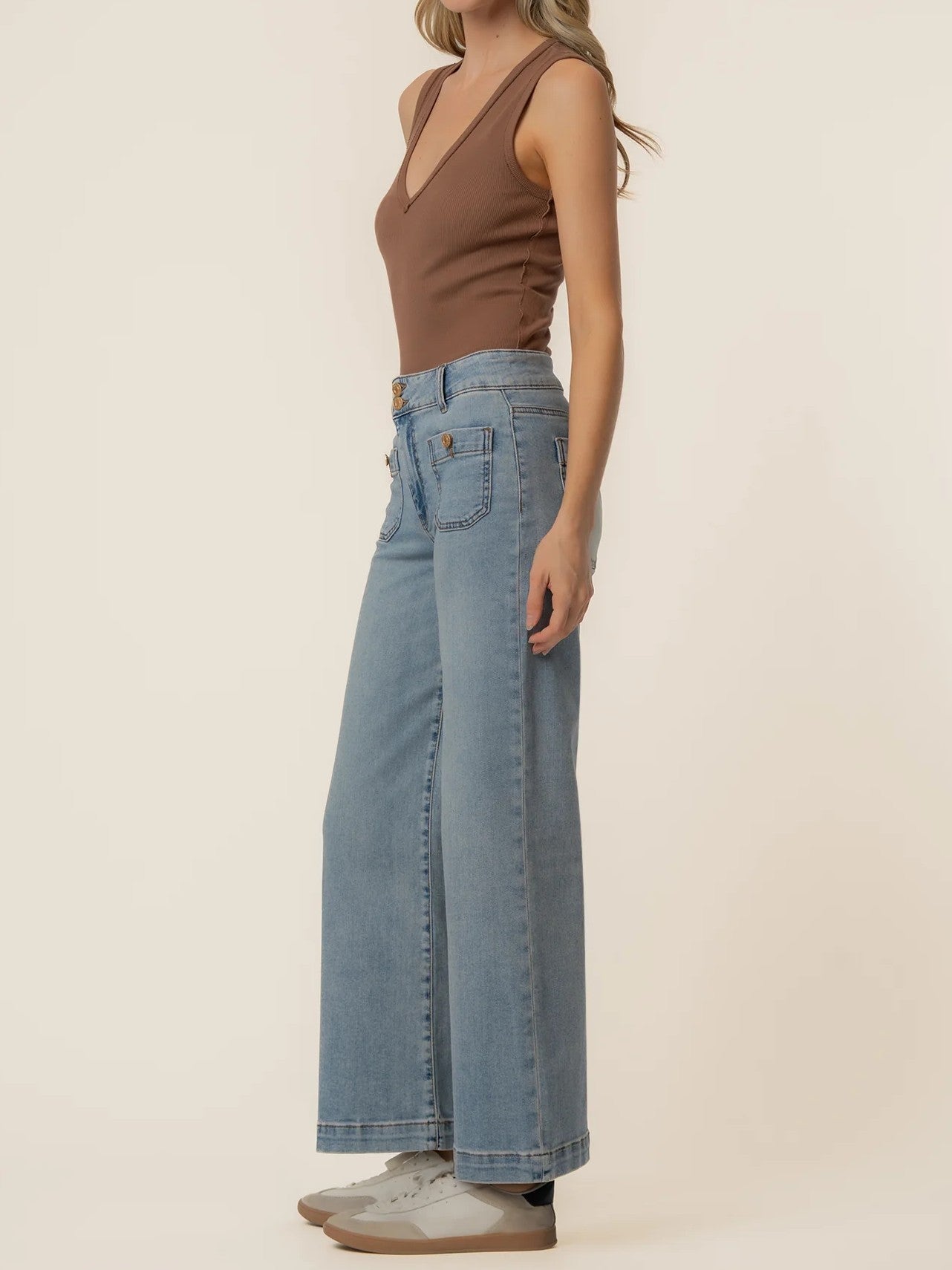 Light blue wide-leg denim jeans paired with a brown sleeveless V-neck top and white sneakers.