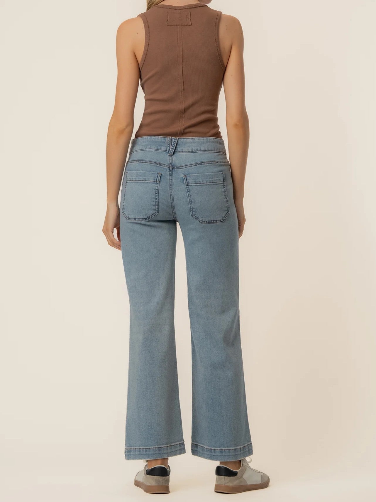 Slim fit light blue denim jeans with rear pockets paired with a brown sleeveless top and casual sneakers