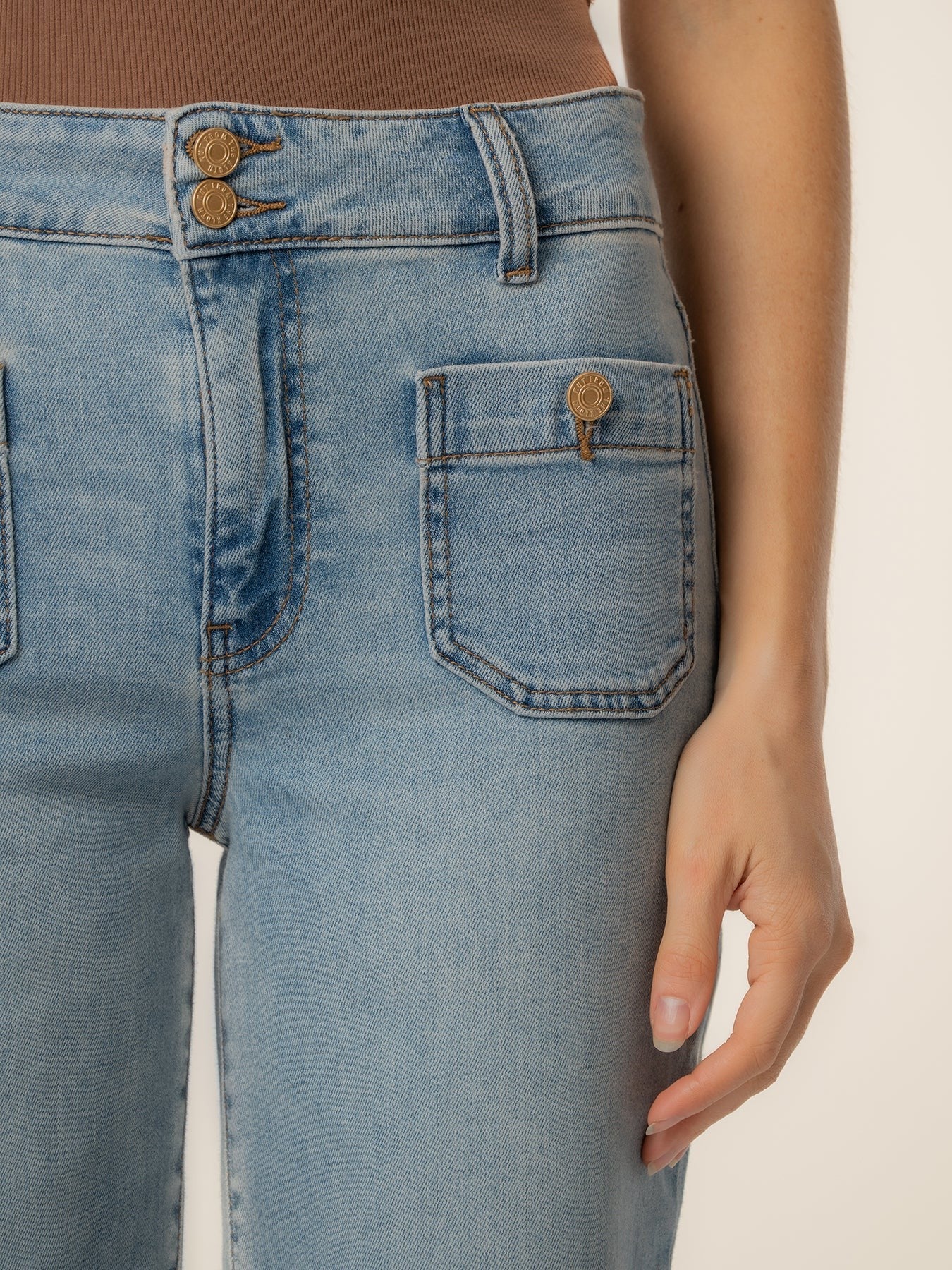 Close-up of light blue denim jeans with high waist, double button closure, and front patch pockets with button details.