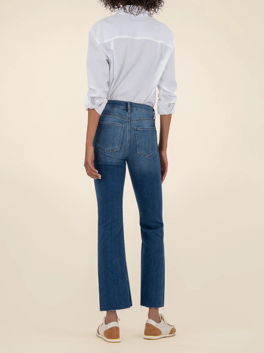 Back view of blue denim Kut from the Kloth Kelsey High Rise Flare Jeans paired with a white shirt and sneakers.