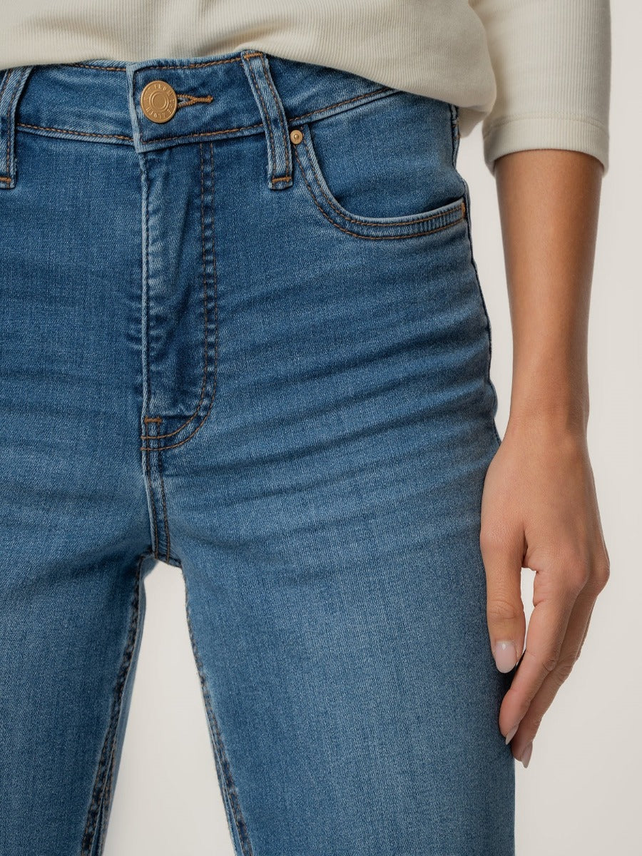 Close-up of blue denim Kut from the Kloth Kelsey High Rise Ankle Flare Jeans with gold button and white top sleeve visible