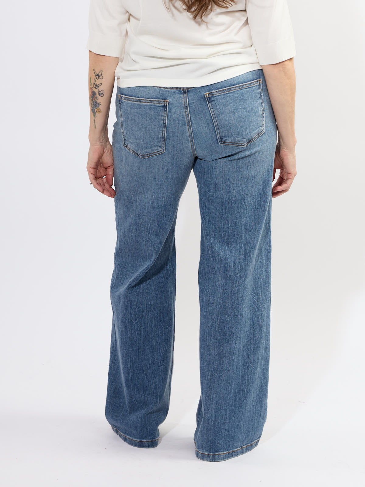 Back view of light blue denim Kut from the Kloth High Rise Jean on a model with a white top and visible arm tattoo.