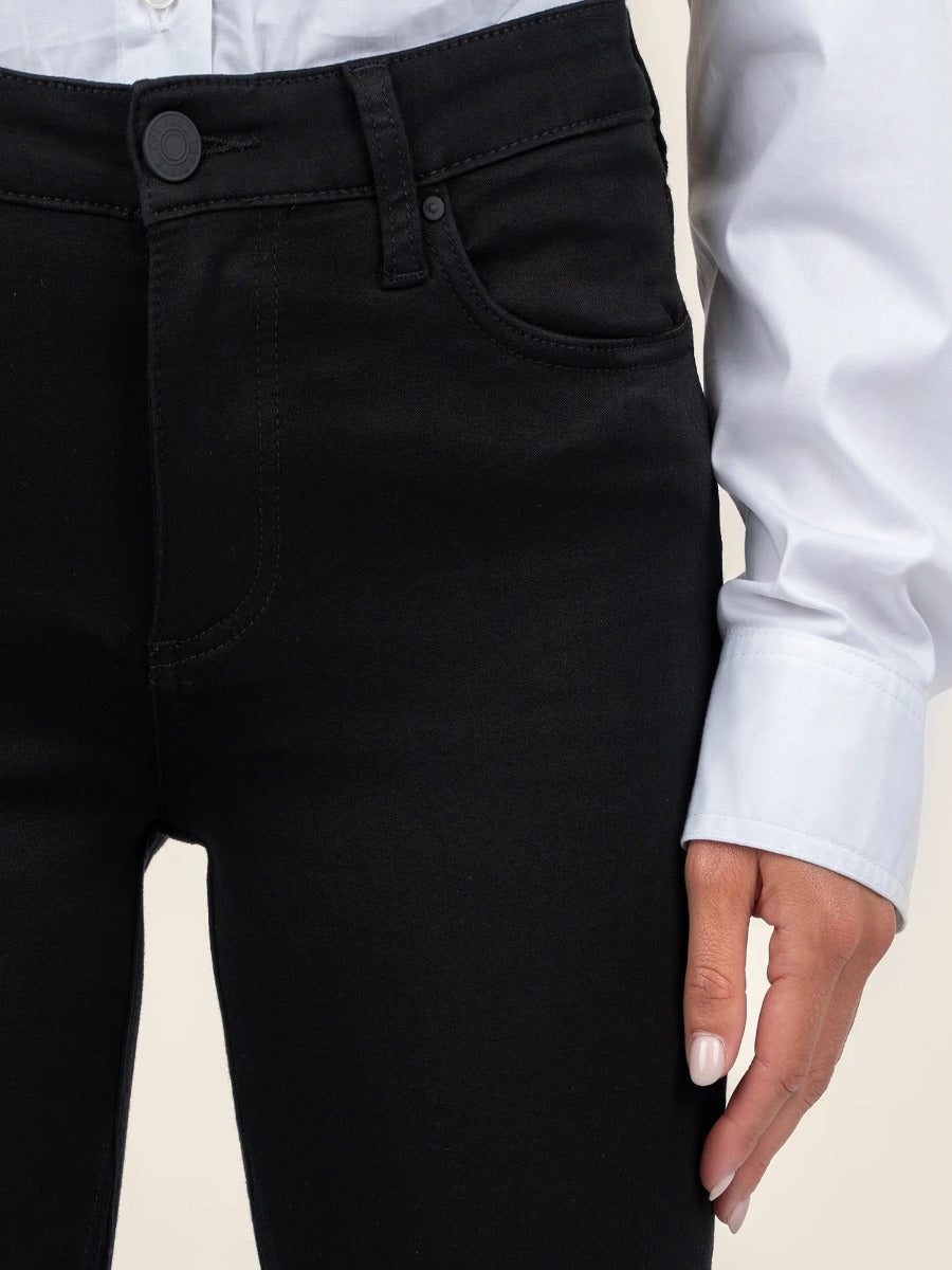 Close-up of black denim Kut from the Kloth Kelsey Mid Rise Flare Jeans with a white shirt sleeve and hand visible