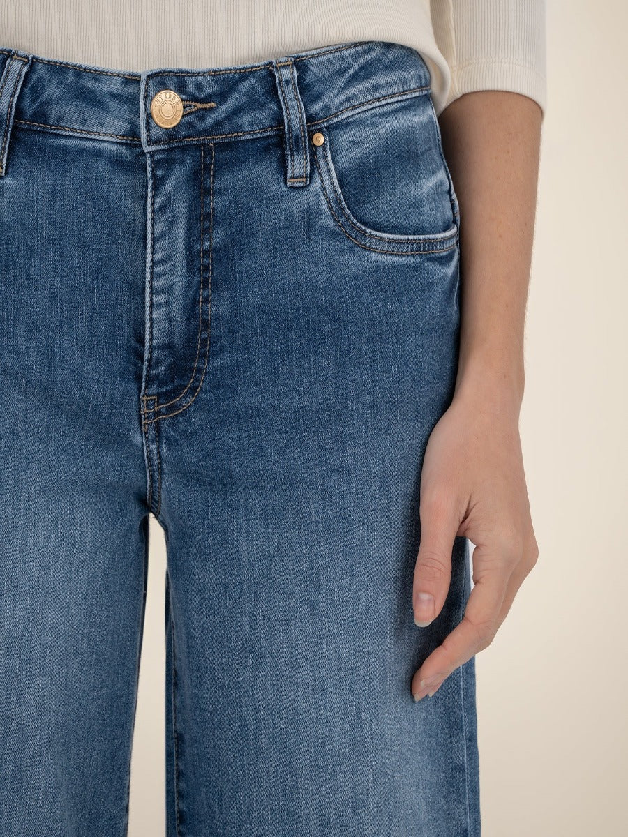 Close-up of blue denim Kut from the Kloth Maya High Rise 31” Wide Leg Trousers with a hand resting beside the leg