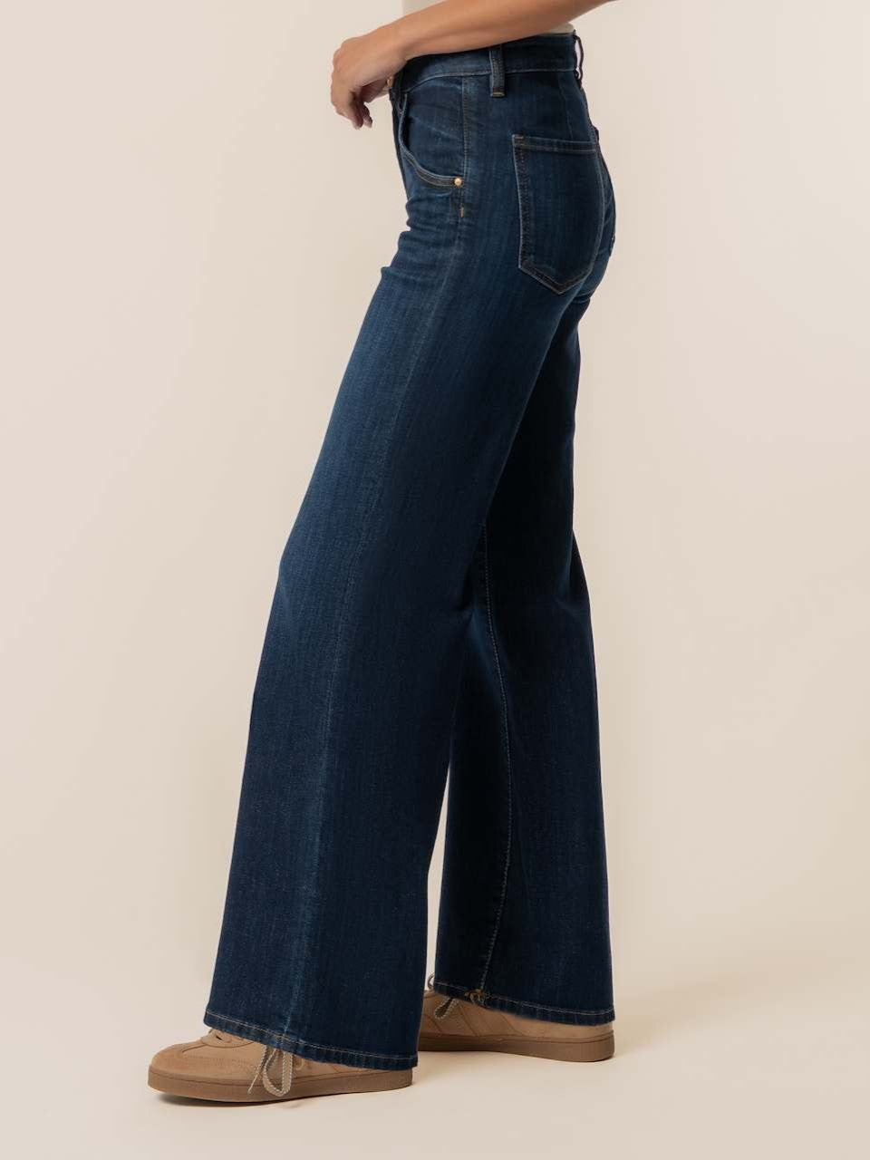 Side view of dark blue wide-leg denim jeans with front and back pockets and tan shoes