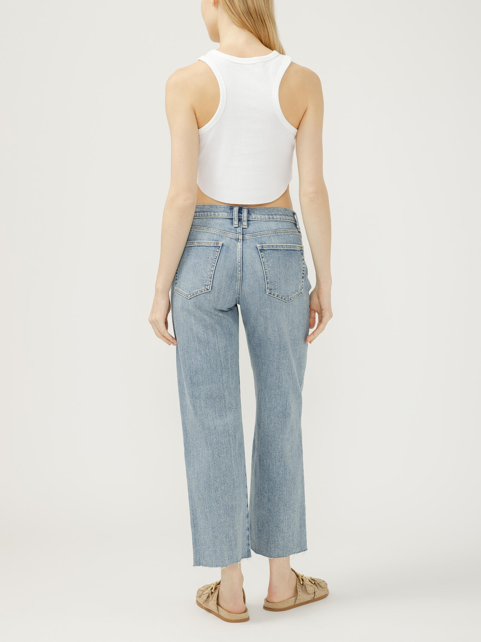 Rear view of light blue straight-leg denim jeans paired with a white cropped racerback top and beige slip-on sandals.