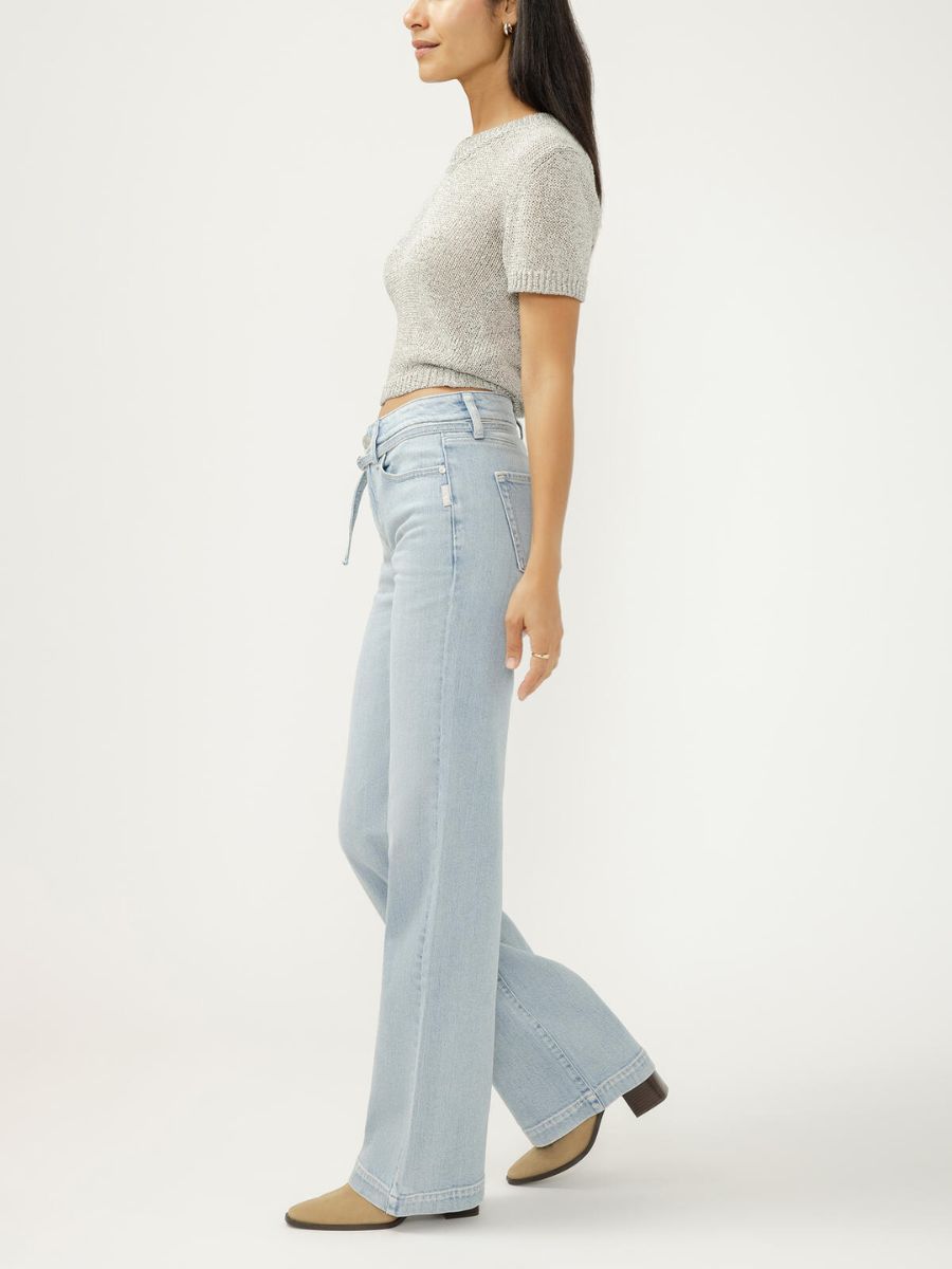 Side view of person wearing a short-sleeve knit top and light-wash wide-leg denim jeans with beige shoes.
