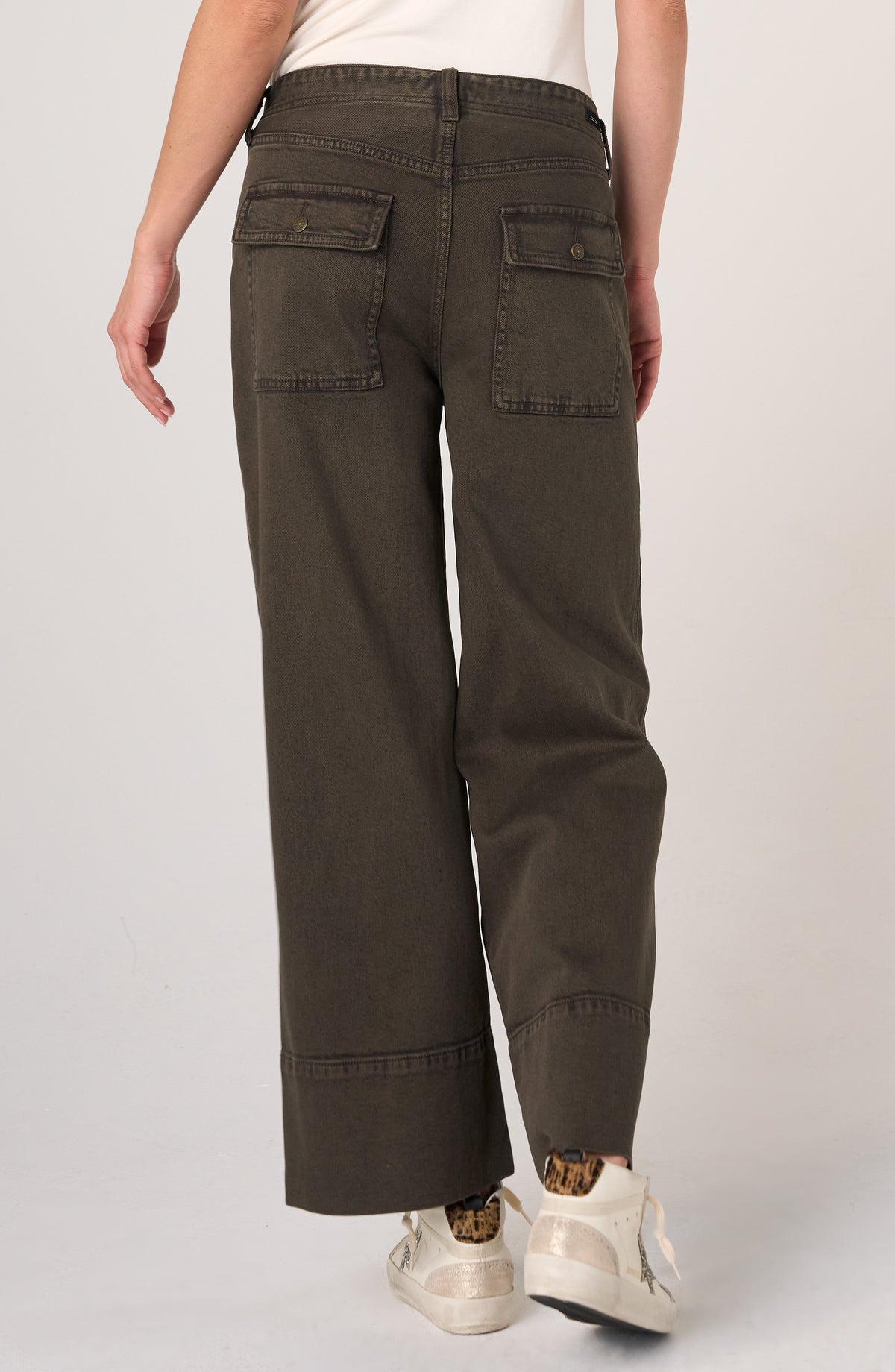 Back view of dark wide-leg denim pants with large flap pockets and white sneakers with leopard print accents