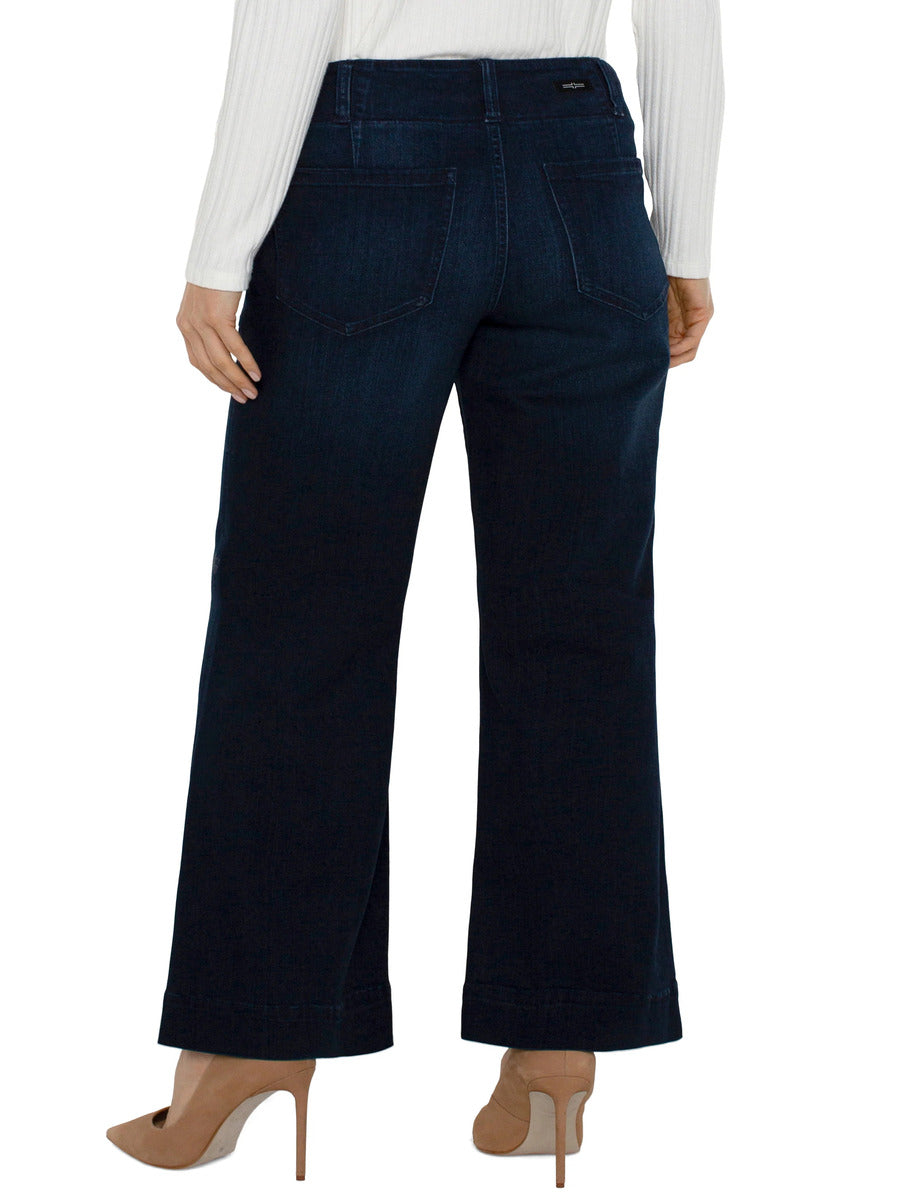 Back view of wide-leg dark denim jeans paired with beige high-heeled shoes and a white long-sleeve top.