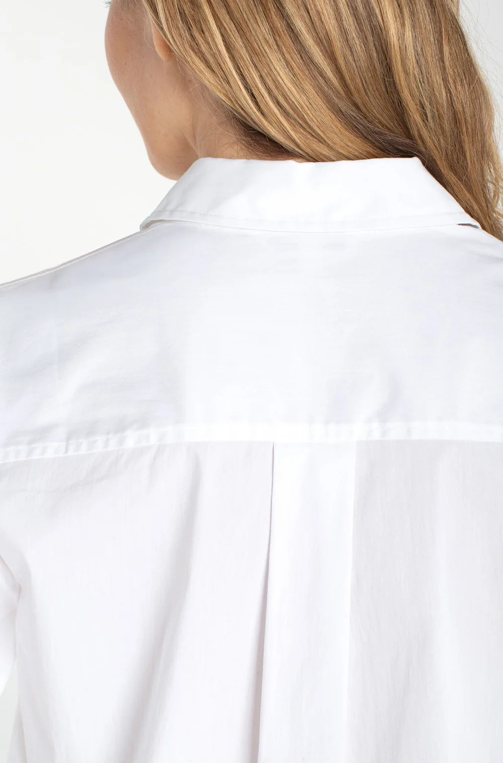 Back view of a white collared shirt with pleat detail beneath the yoke and blonde hair visible against a white background