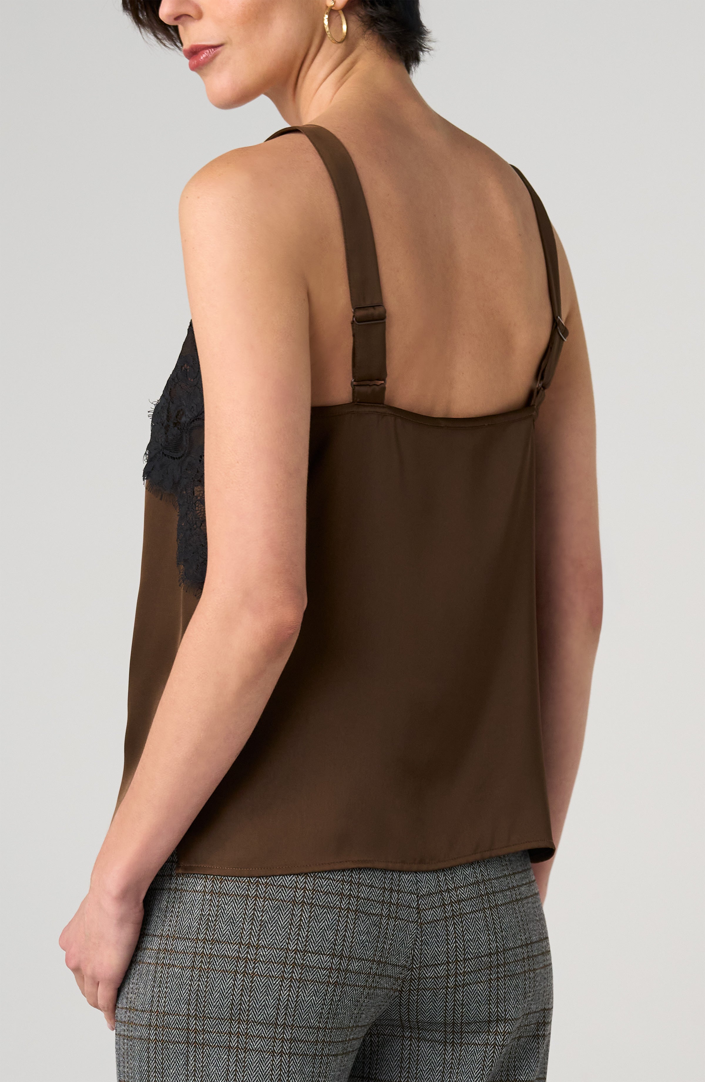 Back view of a brown sleeveless top with adjustable straps and black lace detail paired with gray plaid trousers