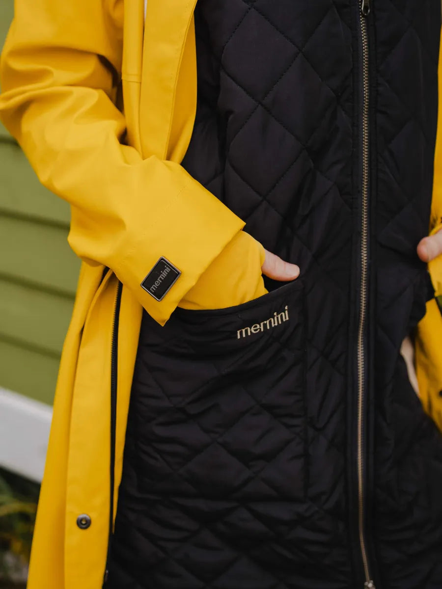 Close-up of a yellow coat sleeve and black quilted jacket pocket with "merrini" branding embroidered on it.