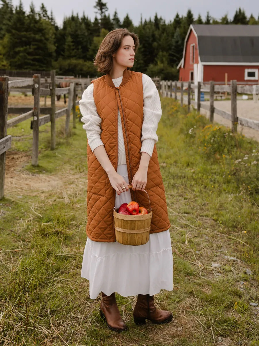 Outdoor rustic scene with a person wearing Mernini Quilted Double Pocket Vest by MERNINI/ROCK RAIN INC holding a basket of apples