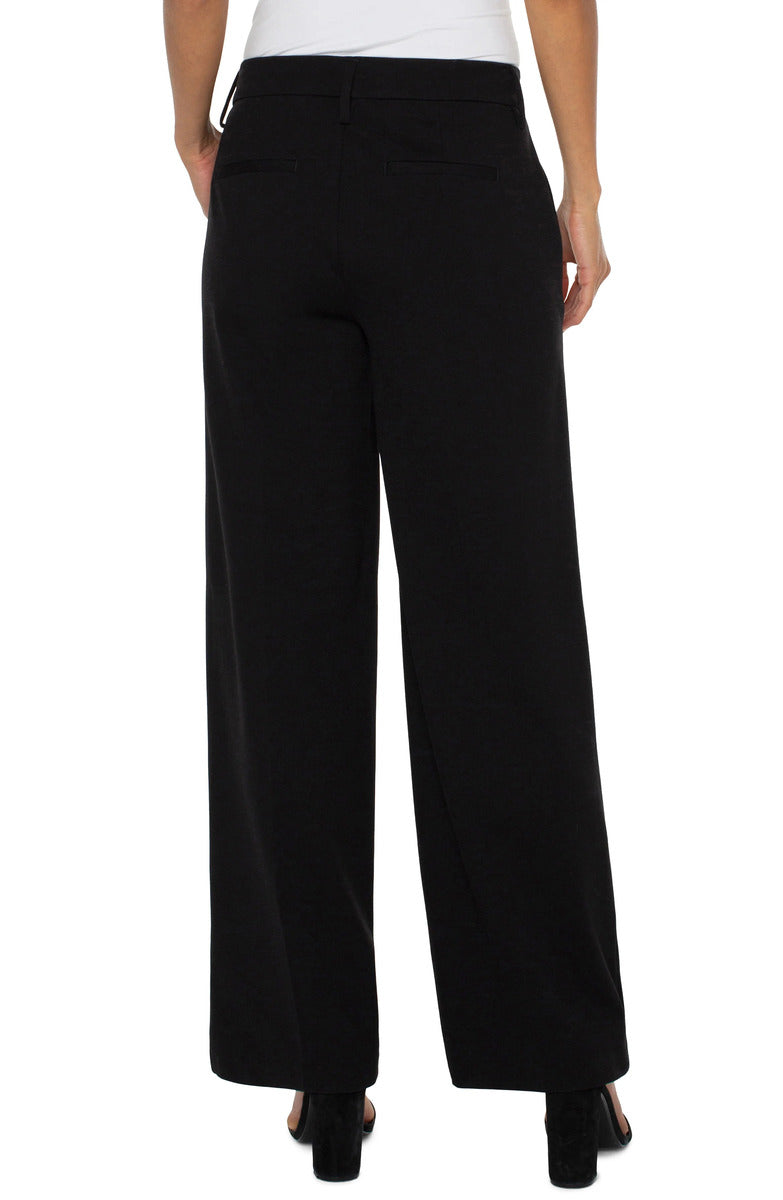 Back view of black Liverpool Kelsey Wide Leg Trouser styled with black heeled shoes and a white top.