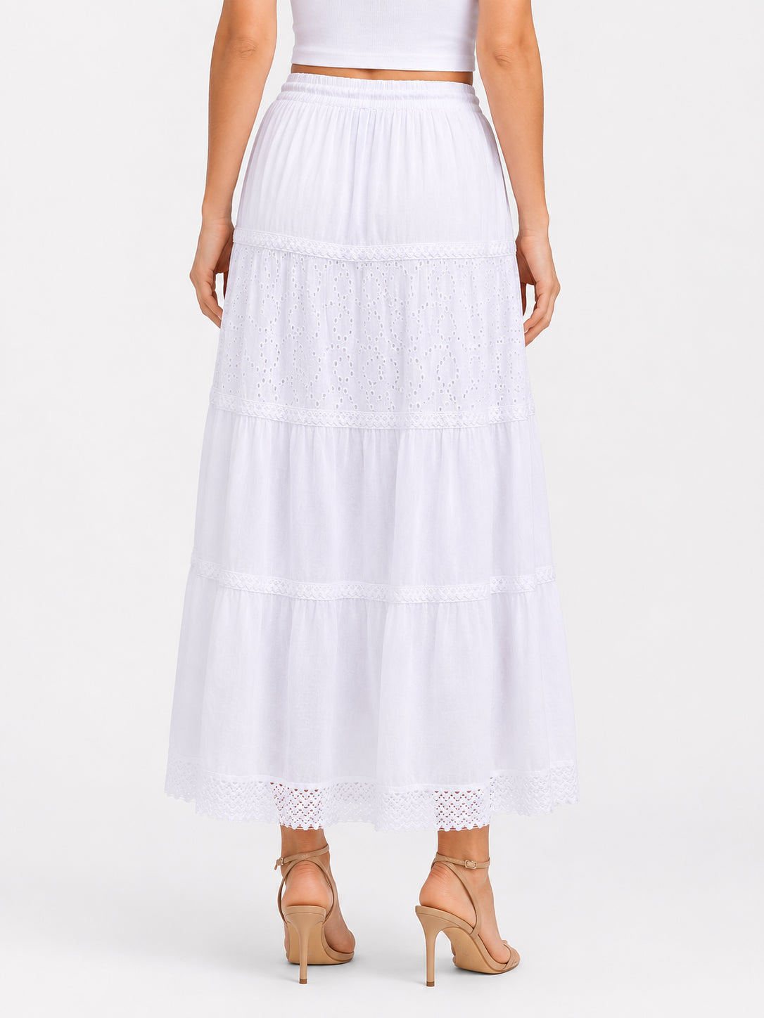 White tiered maxi skirt with eyelet lace details and elastic waistband paired with beige high-heeled sandals.