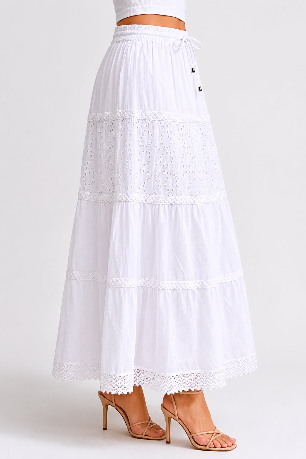 White tiered maxi skirt with eyelet lace detailing and elastic drawstring waist paired with nude heeled sandals