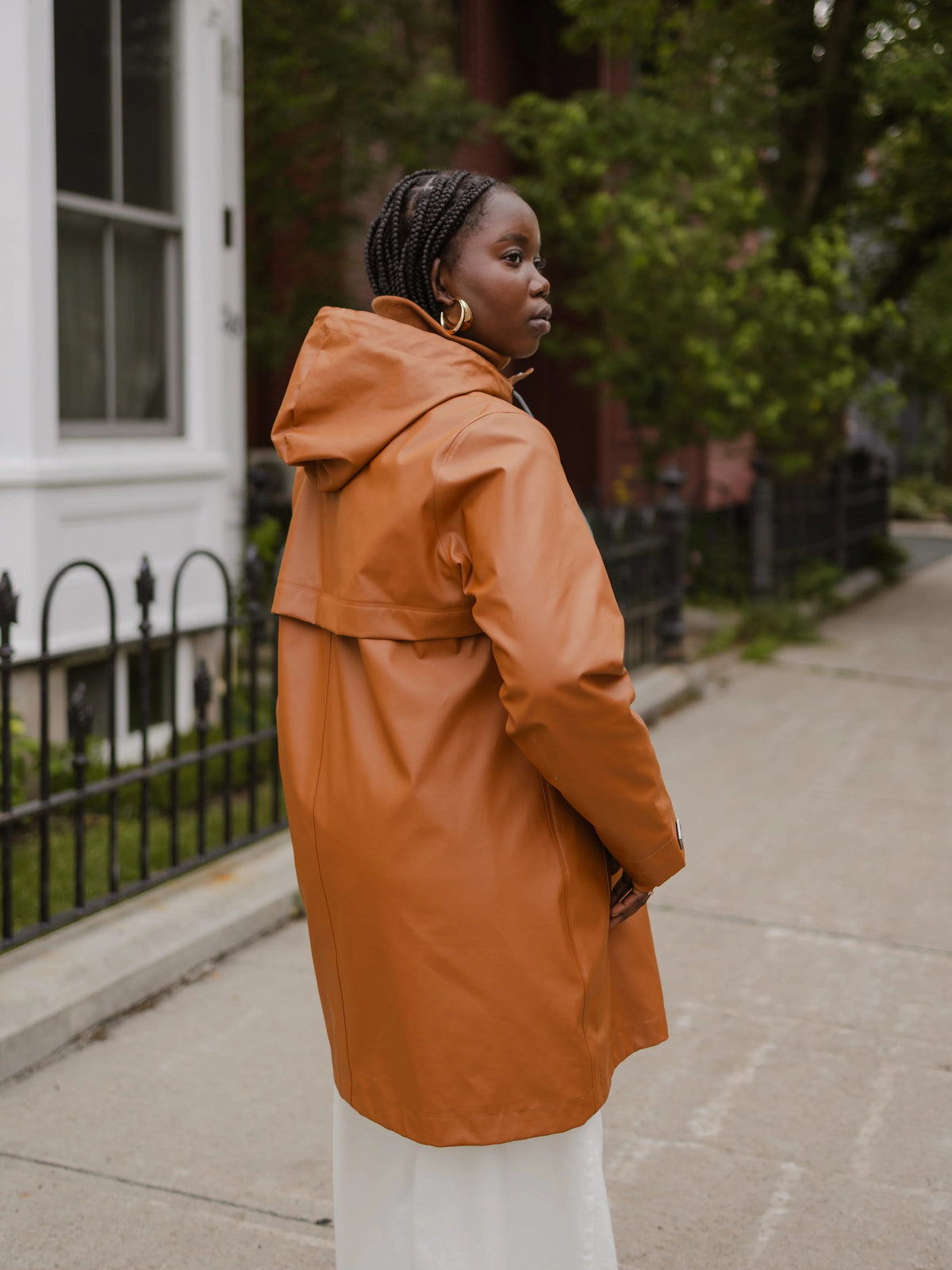 Side view of a woman in a rust orange hooded raincoat on a residential sidewalk