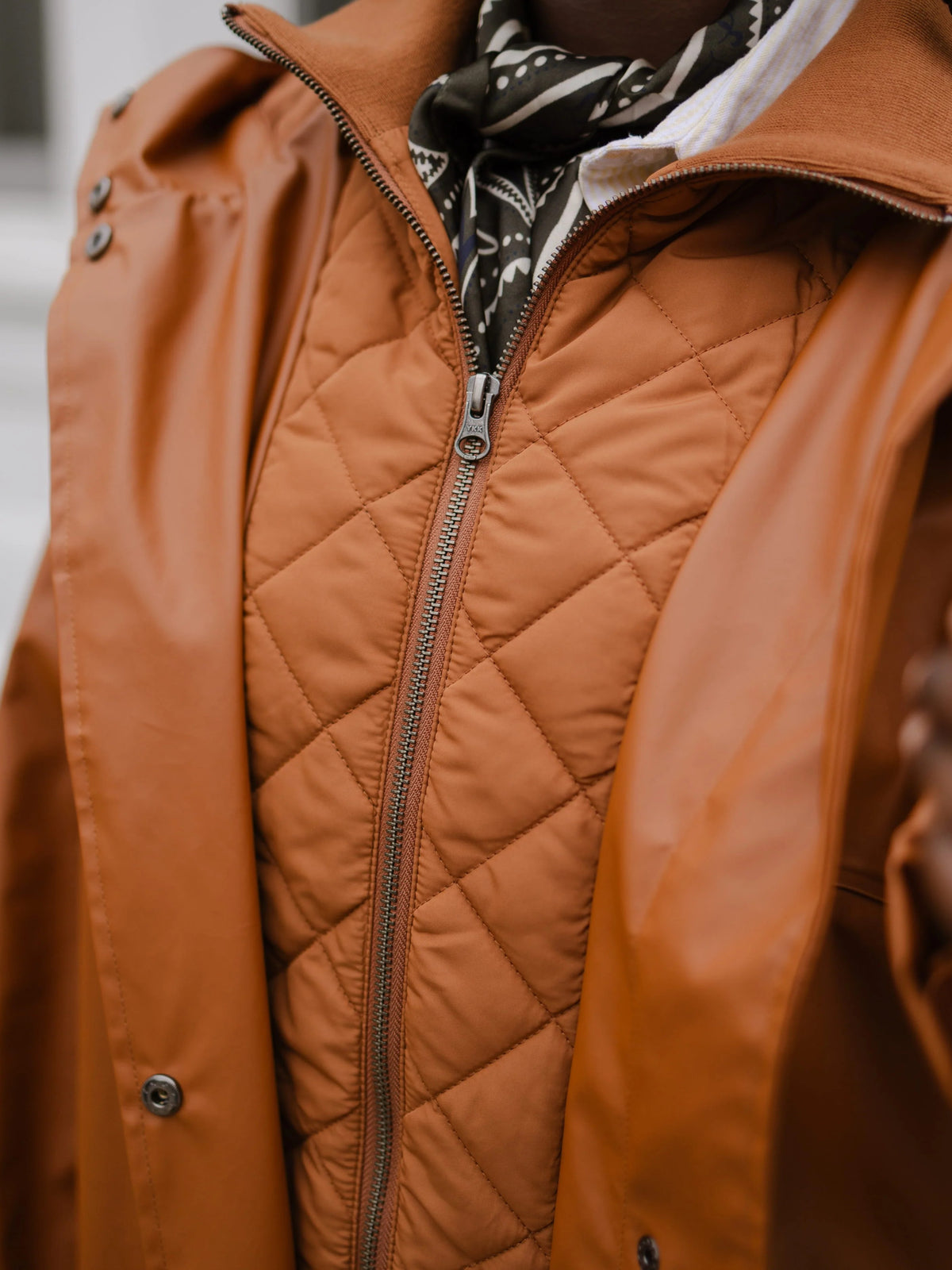 Close-up of a brown quilted jacket with a zip front and patterned scarf