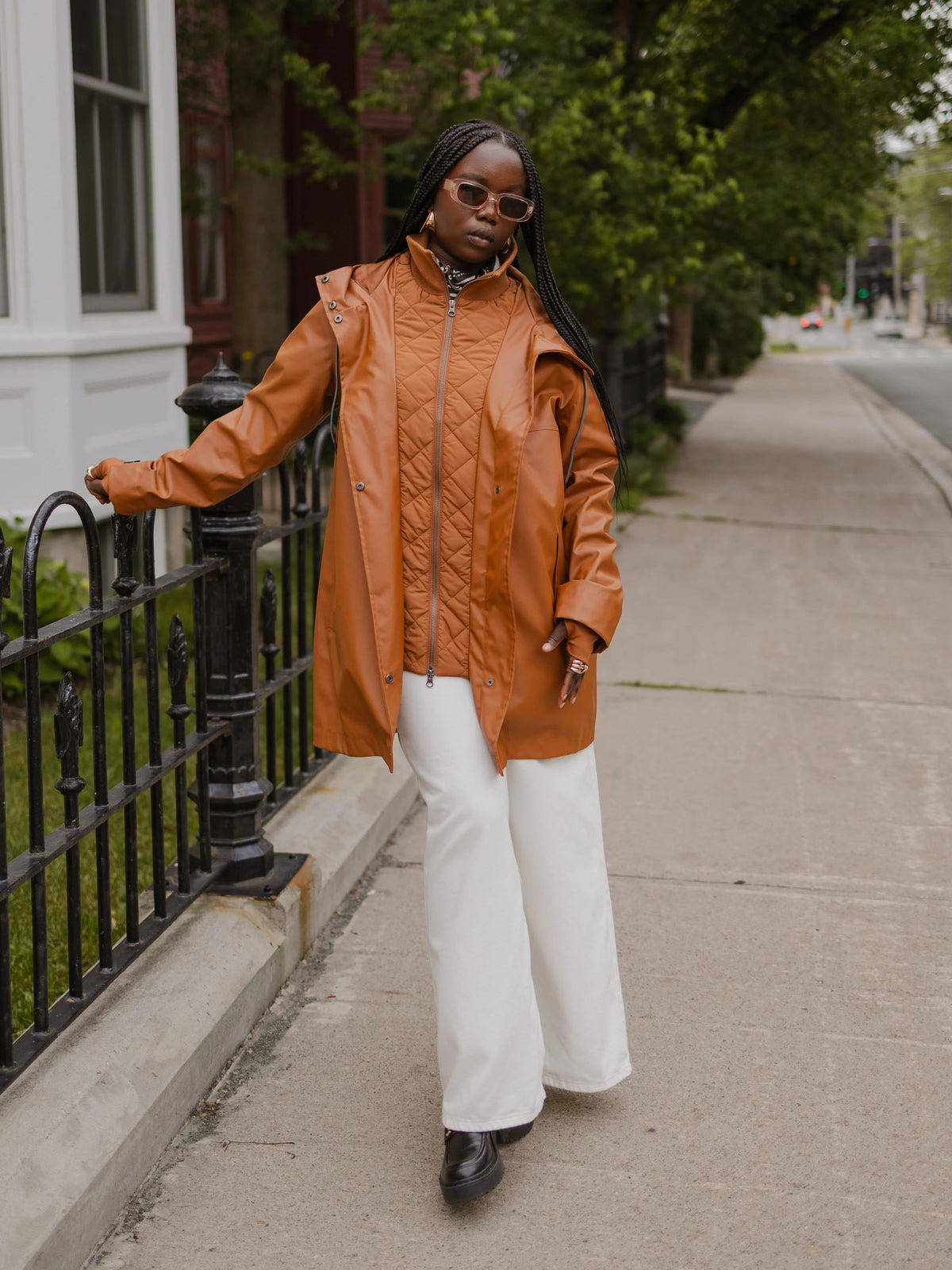 Orange quilted jacket and white trousers on a tree lined city sidewalk