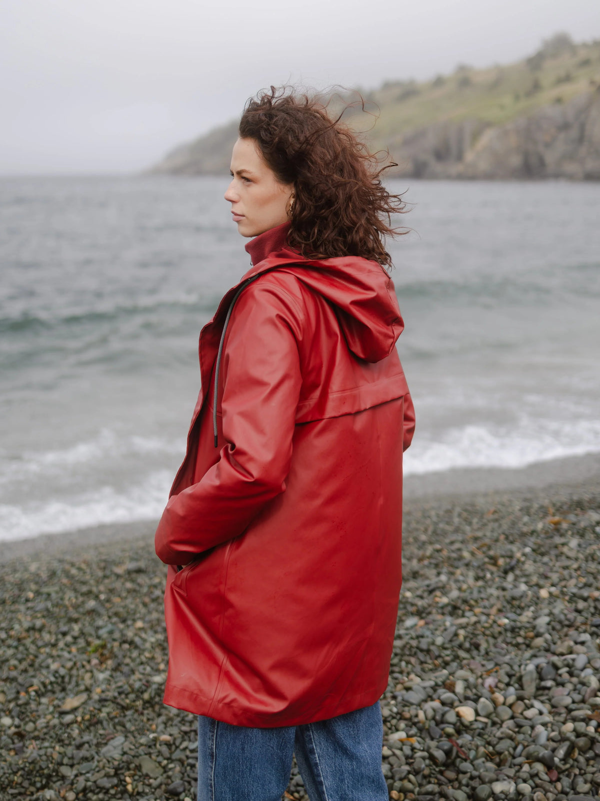 Red hooded rain jacket on a rocky beach beside the sea and coastal cliffs
