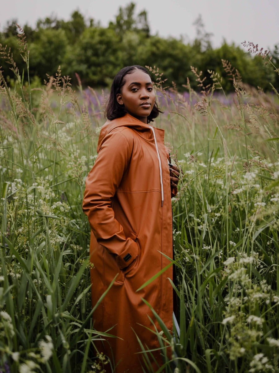 Person standing in a field of tall grass wearing a caramel-colored long coat with a hood