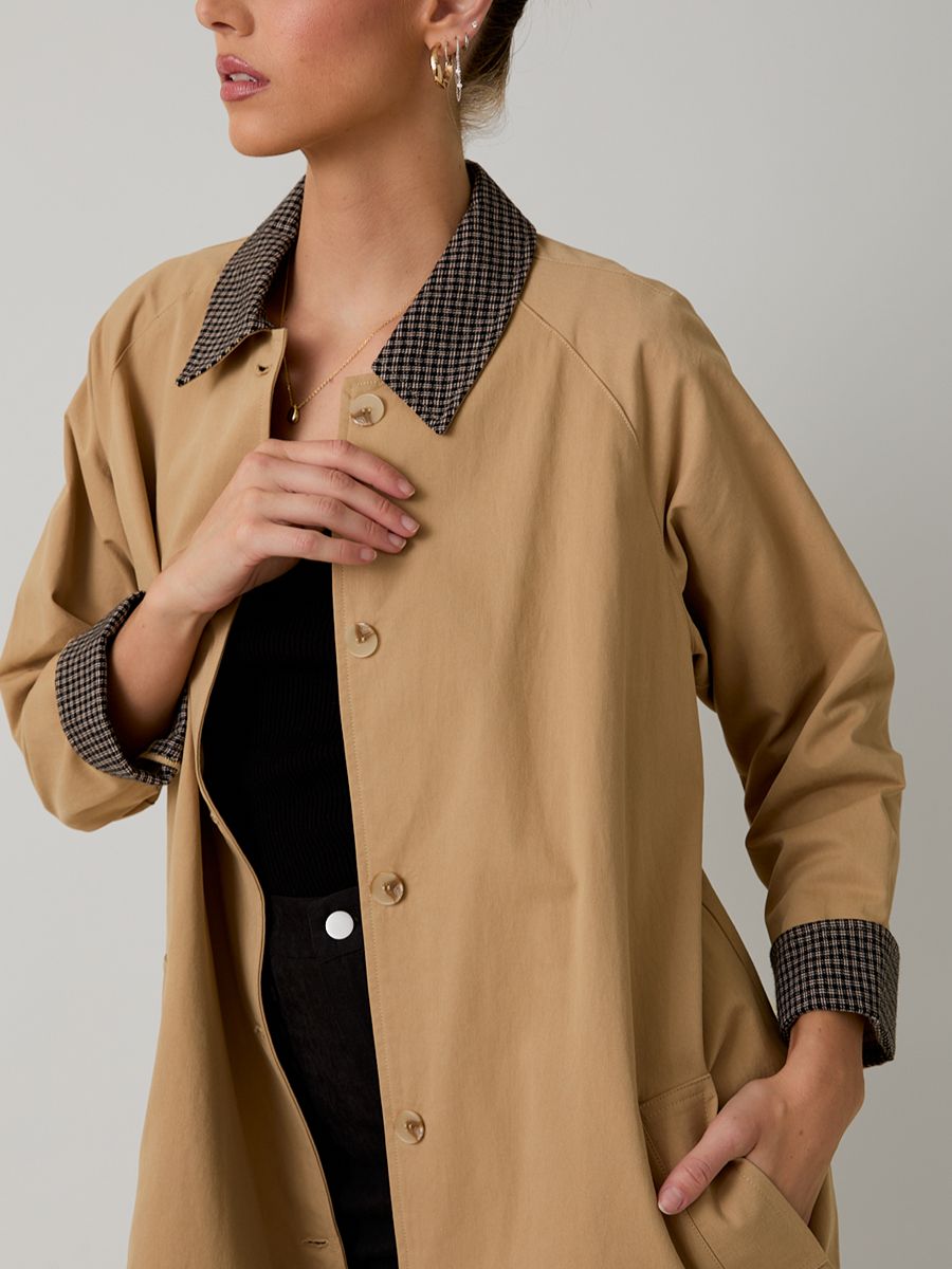 Light brown coat with patterned collar and cuffs over a black top and black pants with a white button detail