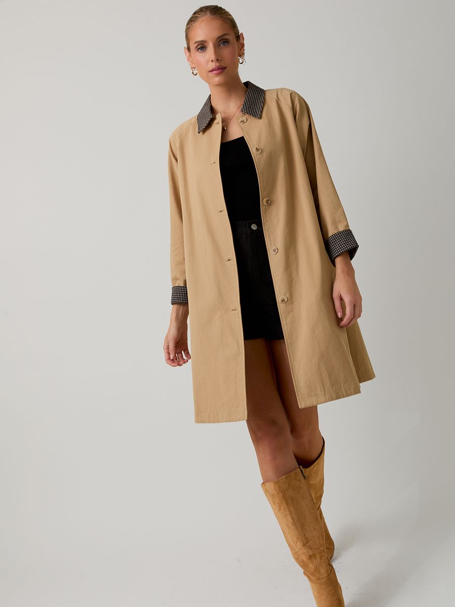 Beige long coat with checked collar and cuffs over black top and skirt, paired with tan suede knee-high boots.
