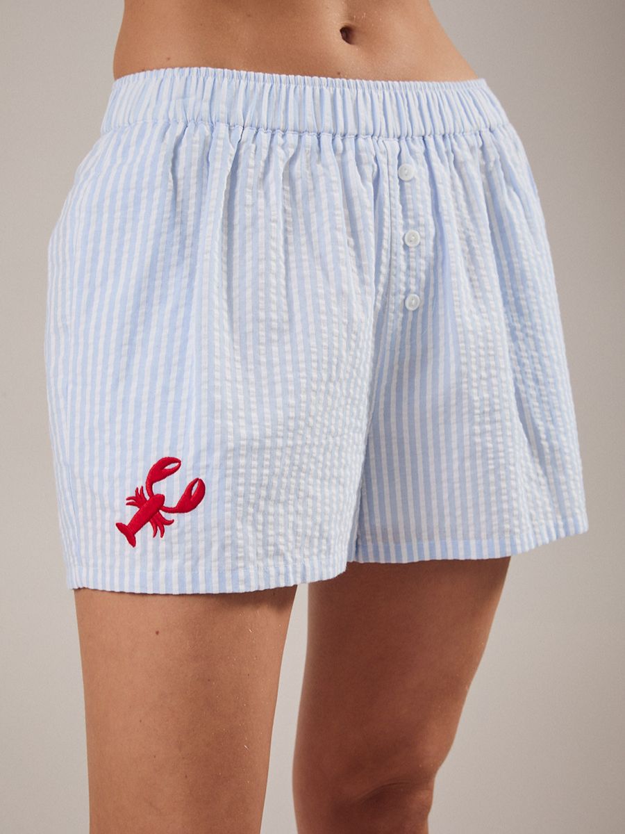 Light blue and white striped shorts with a red embroidered lobster on the left leg and button detail at the waist