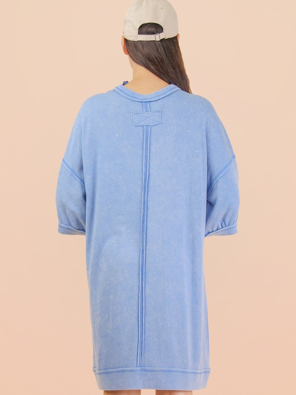 Light blue washed denim oversized short-sleeve dress with raw edge seams and a white baseball cap on neutral background