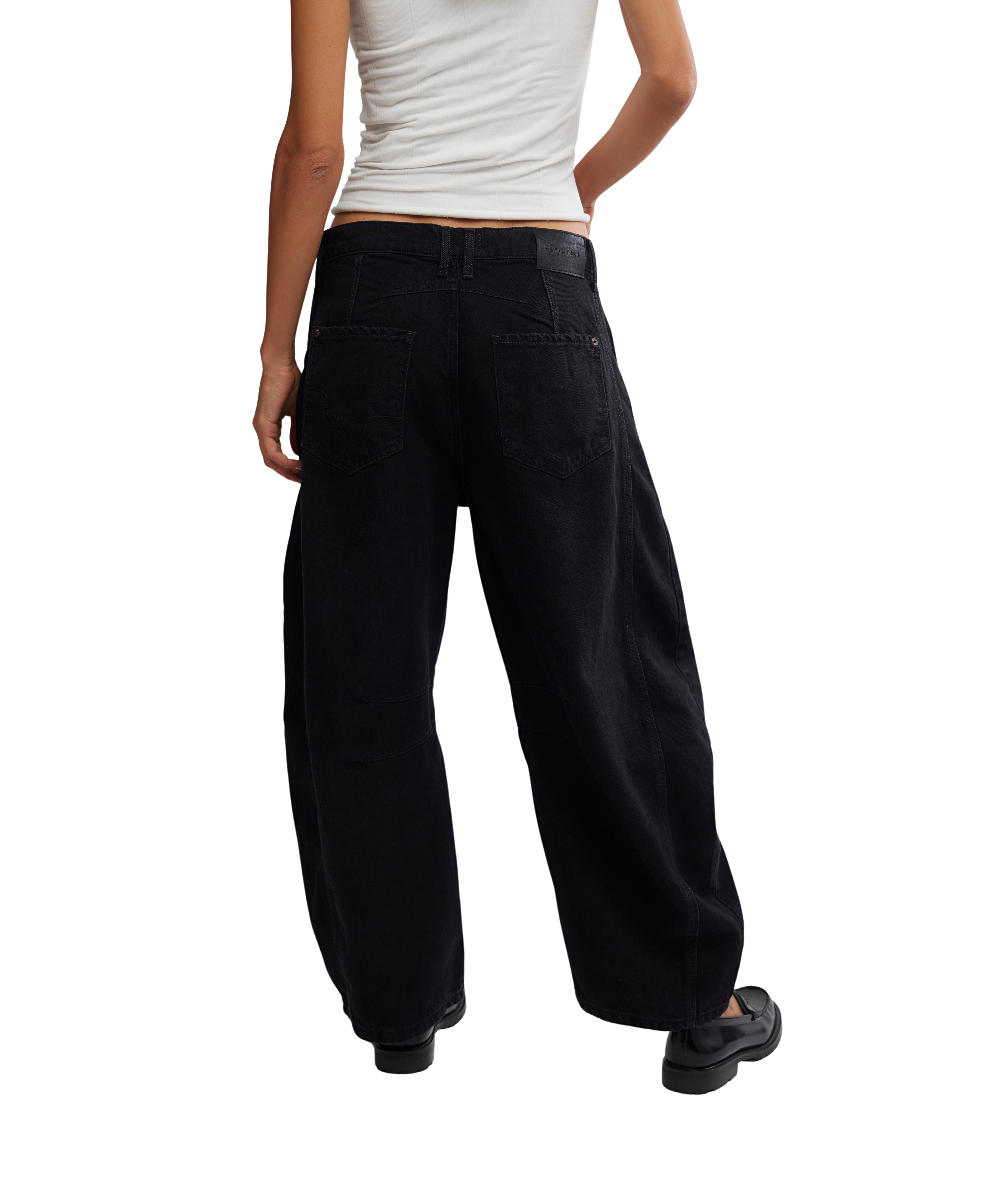 Rear view of black wide-leg Free People Good Luck Black Barrel Denim Jeans paired with a white top and black shoes
