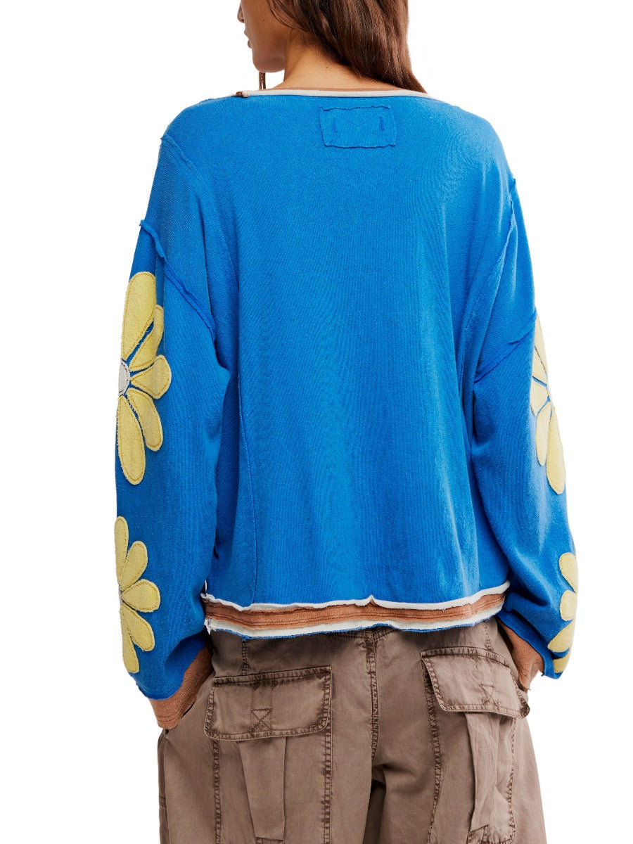 Back view of a blue Free People You’re A Star Floral Top with yellow flower designs on sleeves and brown pants