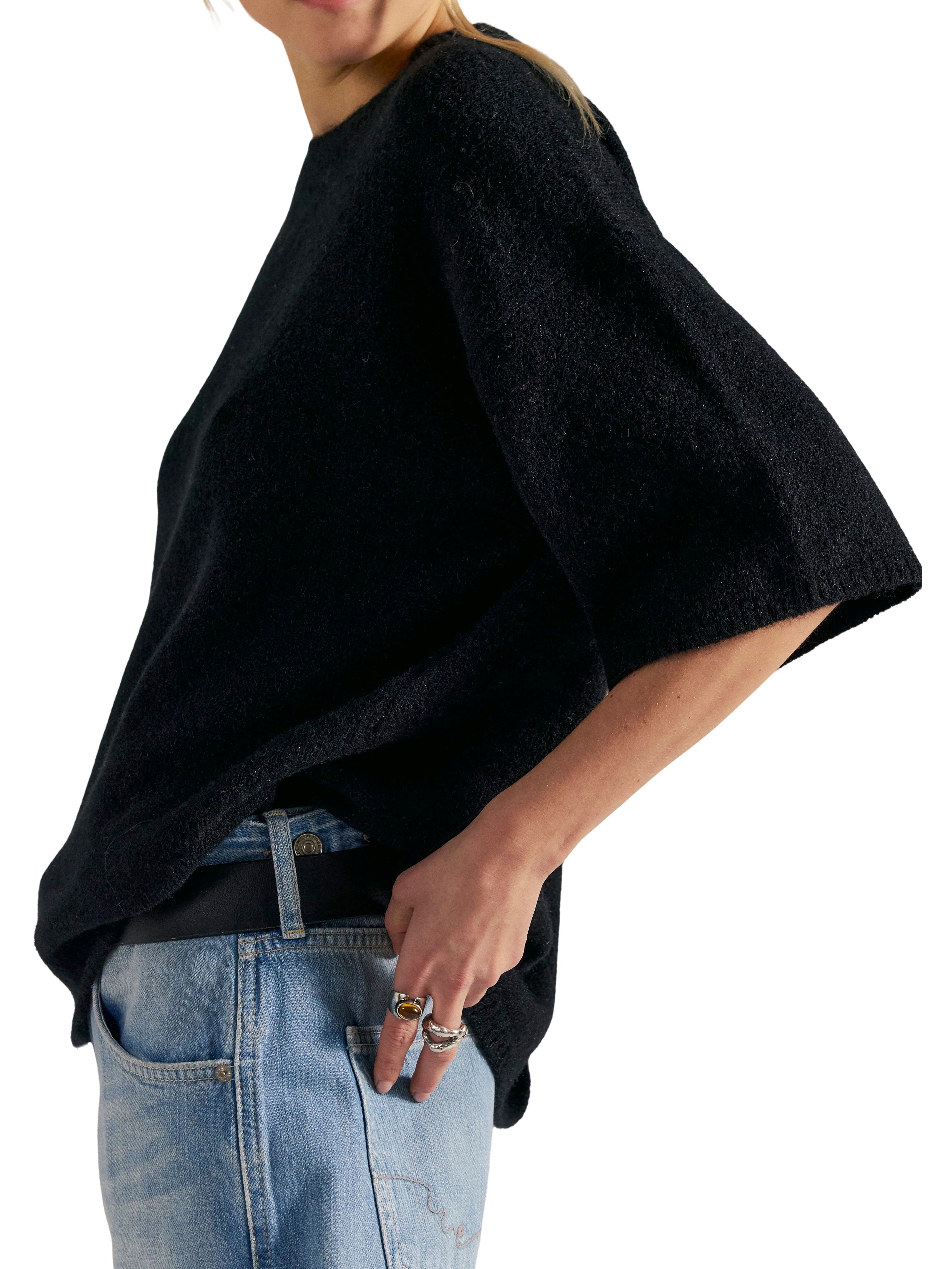 Black textured sweater with elbow-length sleeves paired with light blue denim jeans and multiple rings on hand