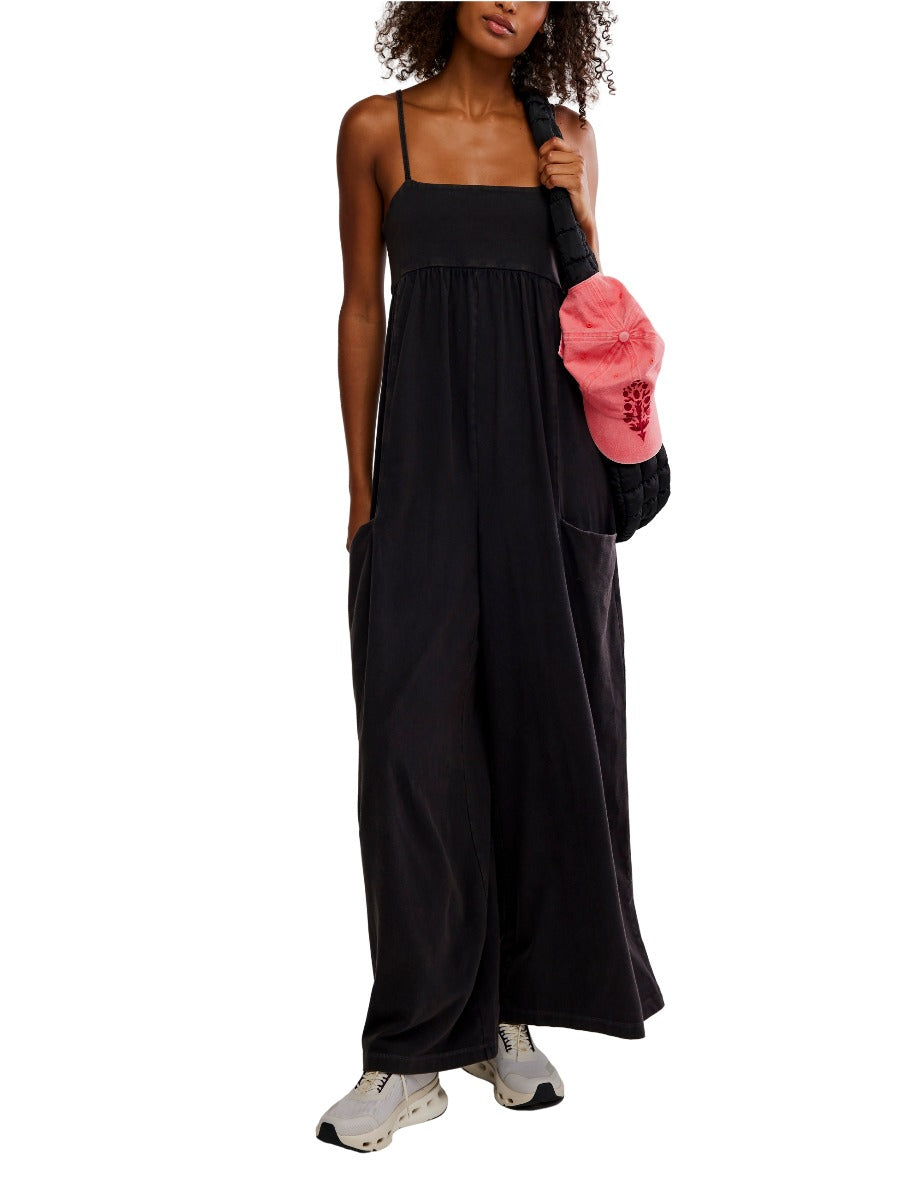 Free People Hot Shot Strappy Onesie in black with wide legs, thin straps, and side pockets styled with sneakers and a bag.