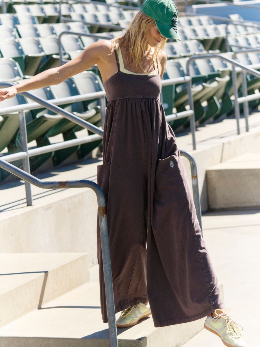 Free People Hot Shot Strappy Onesie in chocolate brown with wide legs and pockets styled with a green cap and sneakers