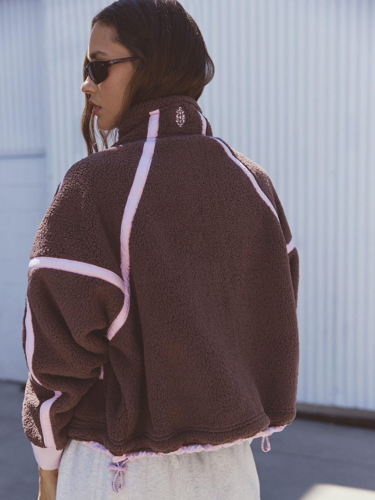 Brown fleece jacket with pink piping and a high collar, shown from the back with sunglasses visible