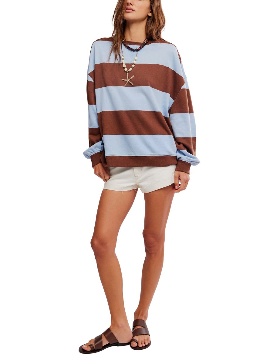 Person wearing a loose striped sweater in blue and brown paired with white shorts, sandals, and layered necklaces