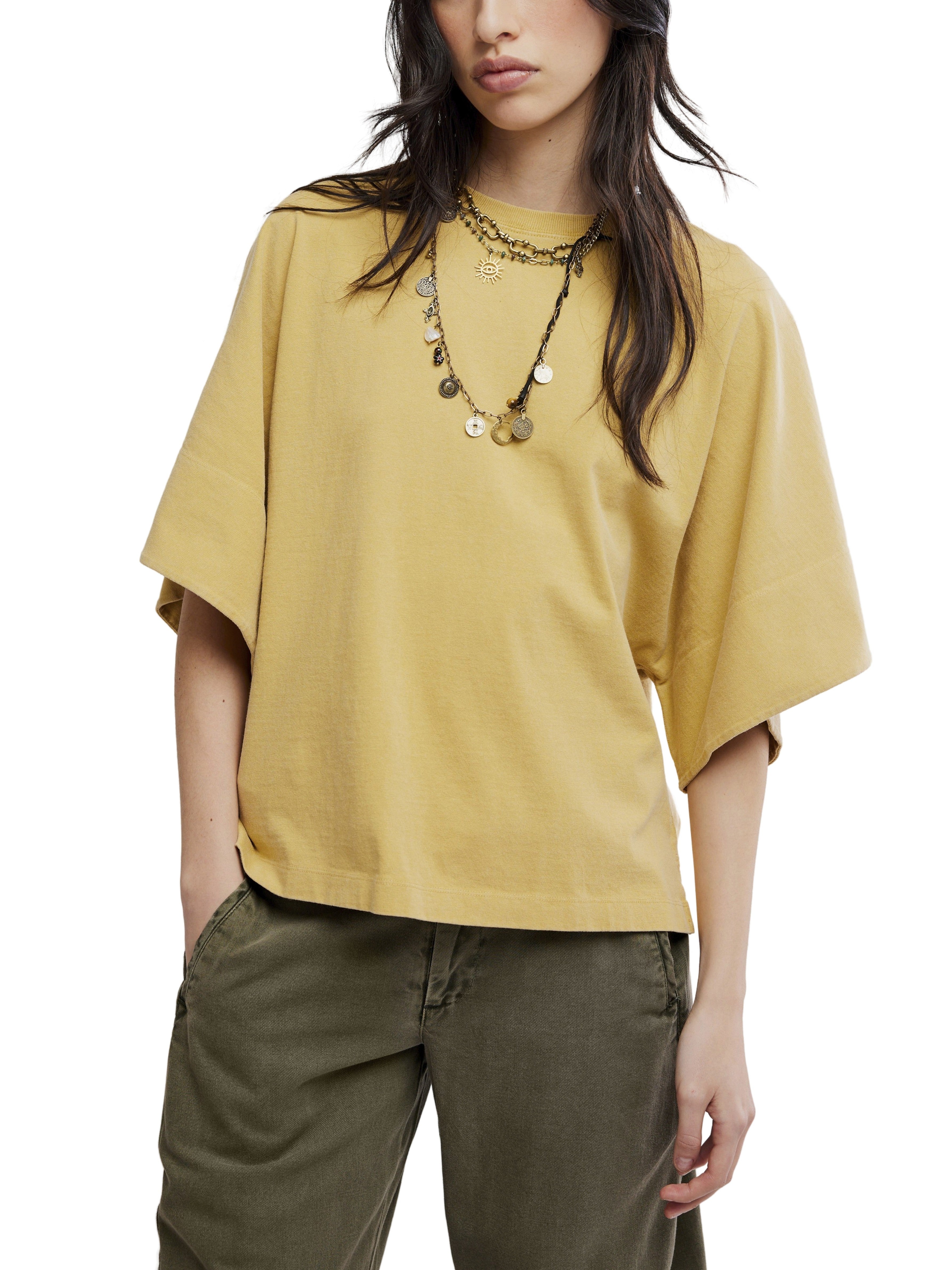 Free People Atlas Dolman Crew Top in muted gold, styled with layered necklaces and green pants by Free People.