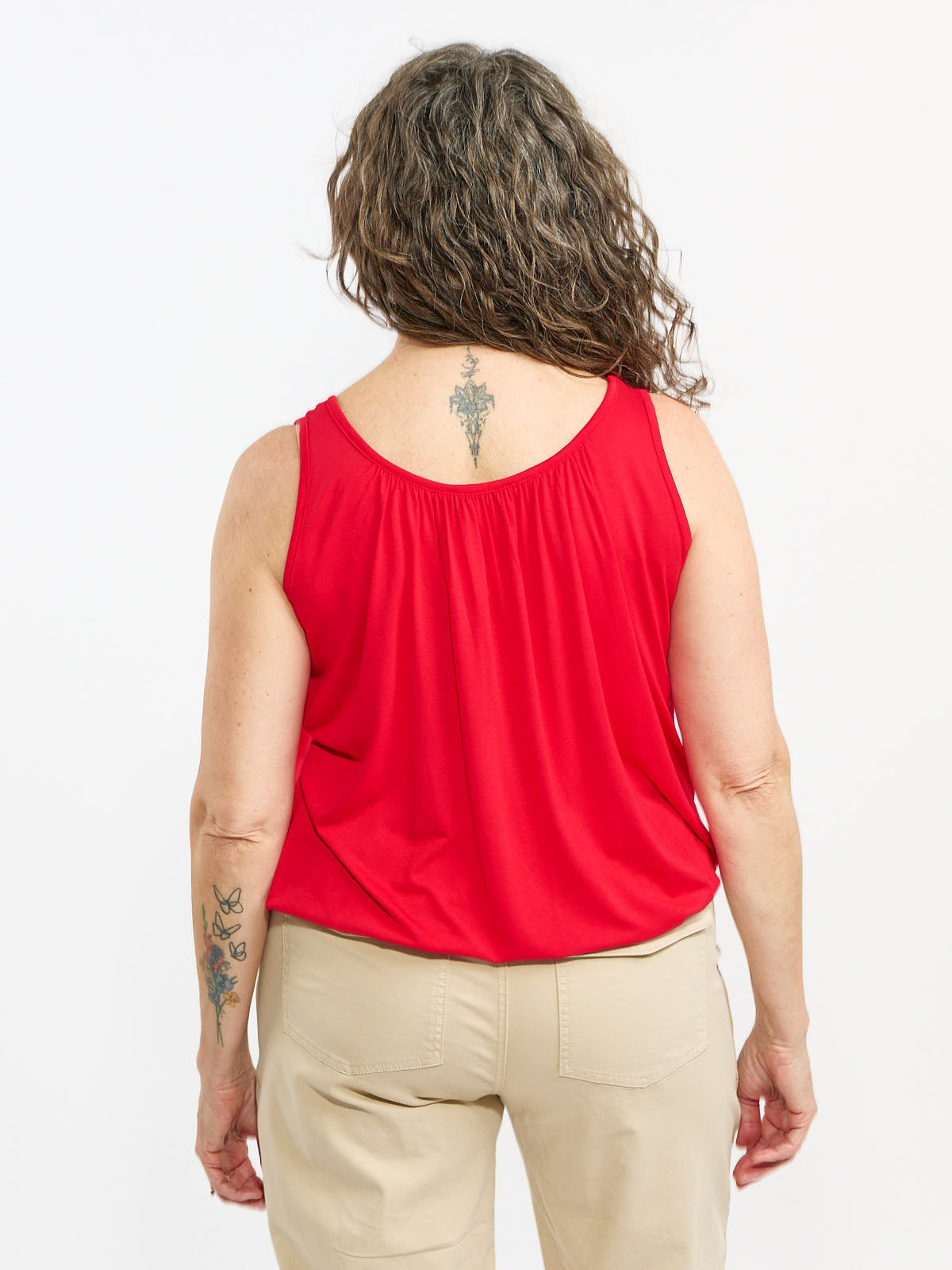 Back view of a red sleeveless top paired with beige pants on a person with curly hair and visible tattoos.