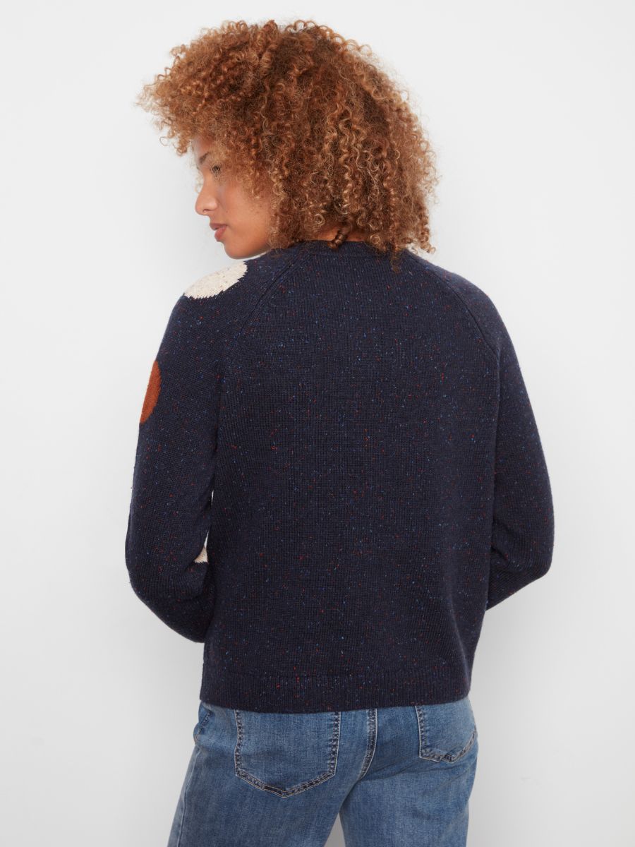 Navy knitted sweater with multicolored elbow patches and subtle speckled detailing paired with blue denim jeans.
