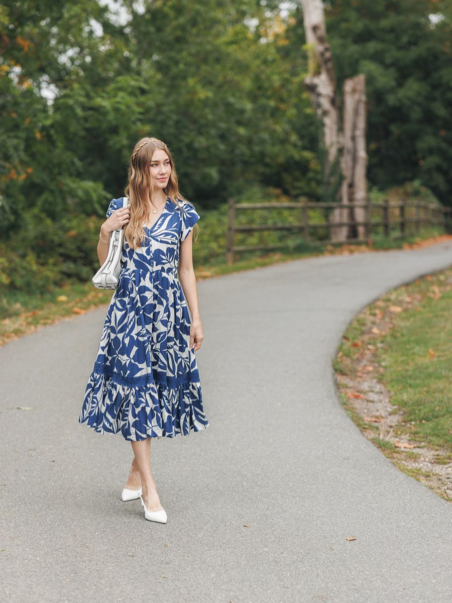 Model in a floral blue dress outdoors on a paved path with greenery, showcasing the Papillon Maxed Out Baby Button Midi Dress