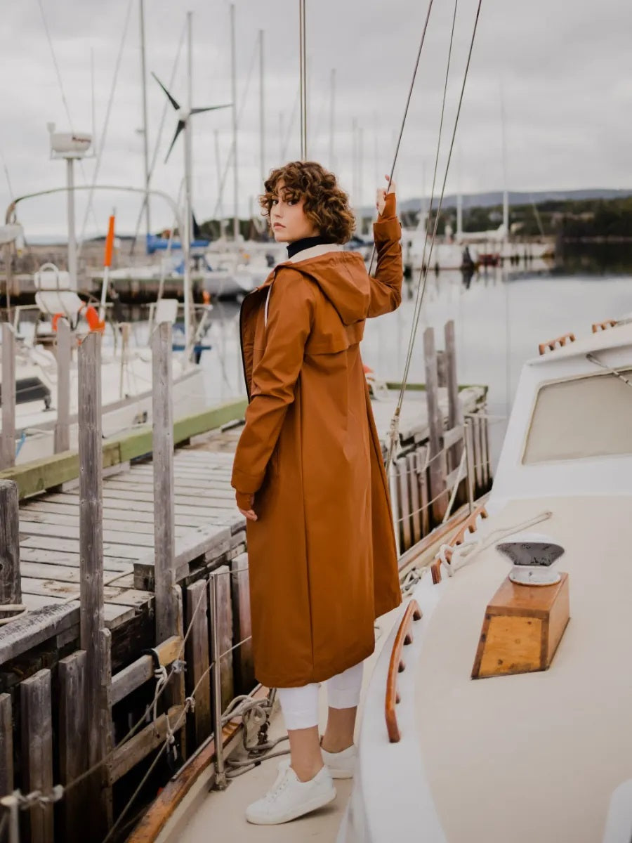 Person near docked boats wearing a caramel Mernini Petite 42” Length Waterproof Raincoat by MERNINI/ROCK RAIN INC